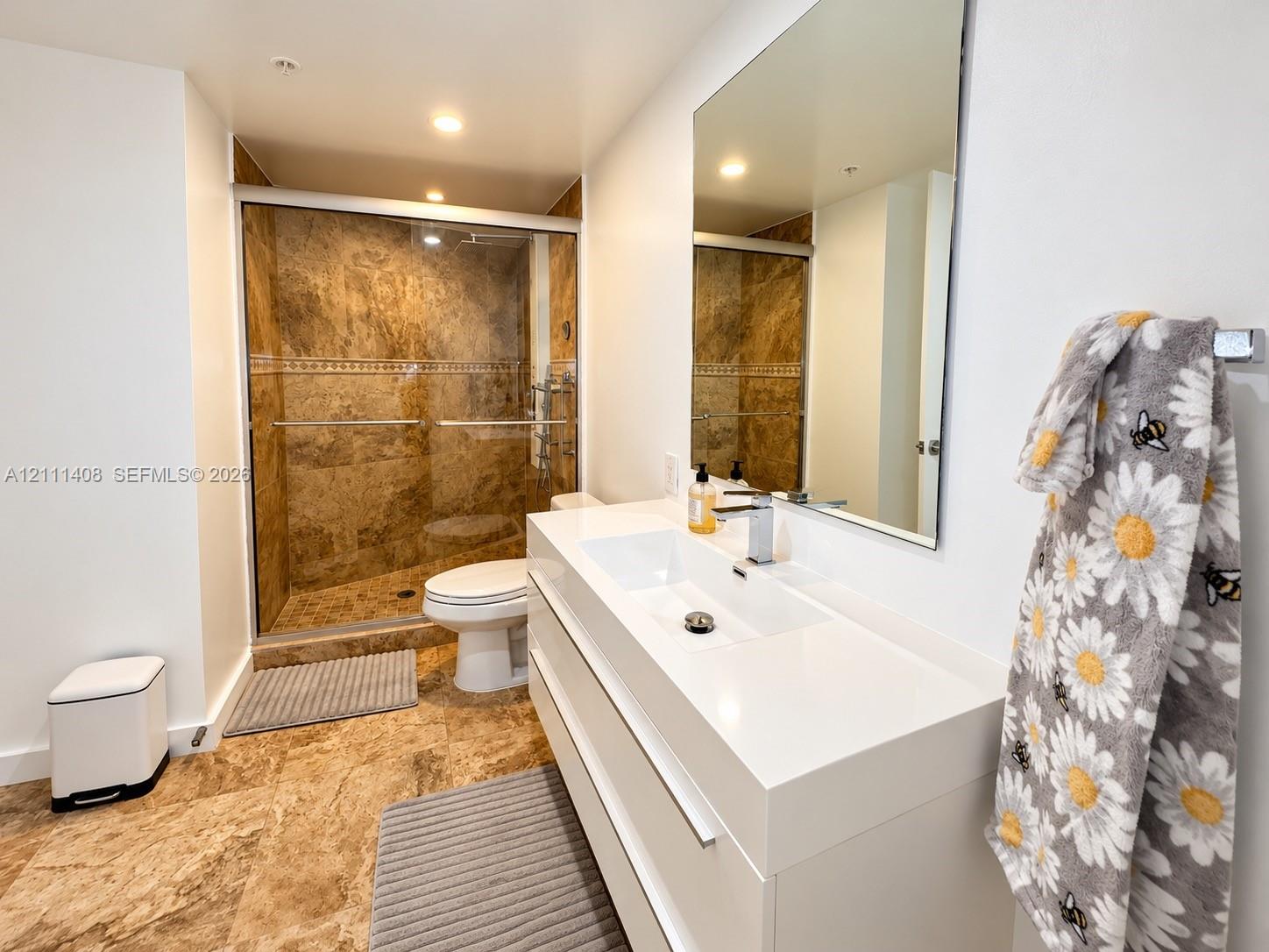 Wood-finish flooring, sliding glass door with balcony access, built-in floor-to-ceiling cabinetry, minimalist geometric flush-mount lighting, and bi-fold closet doors