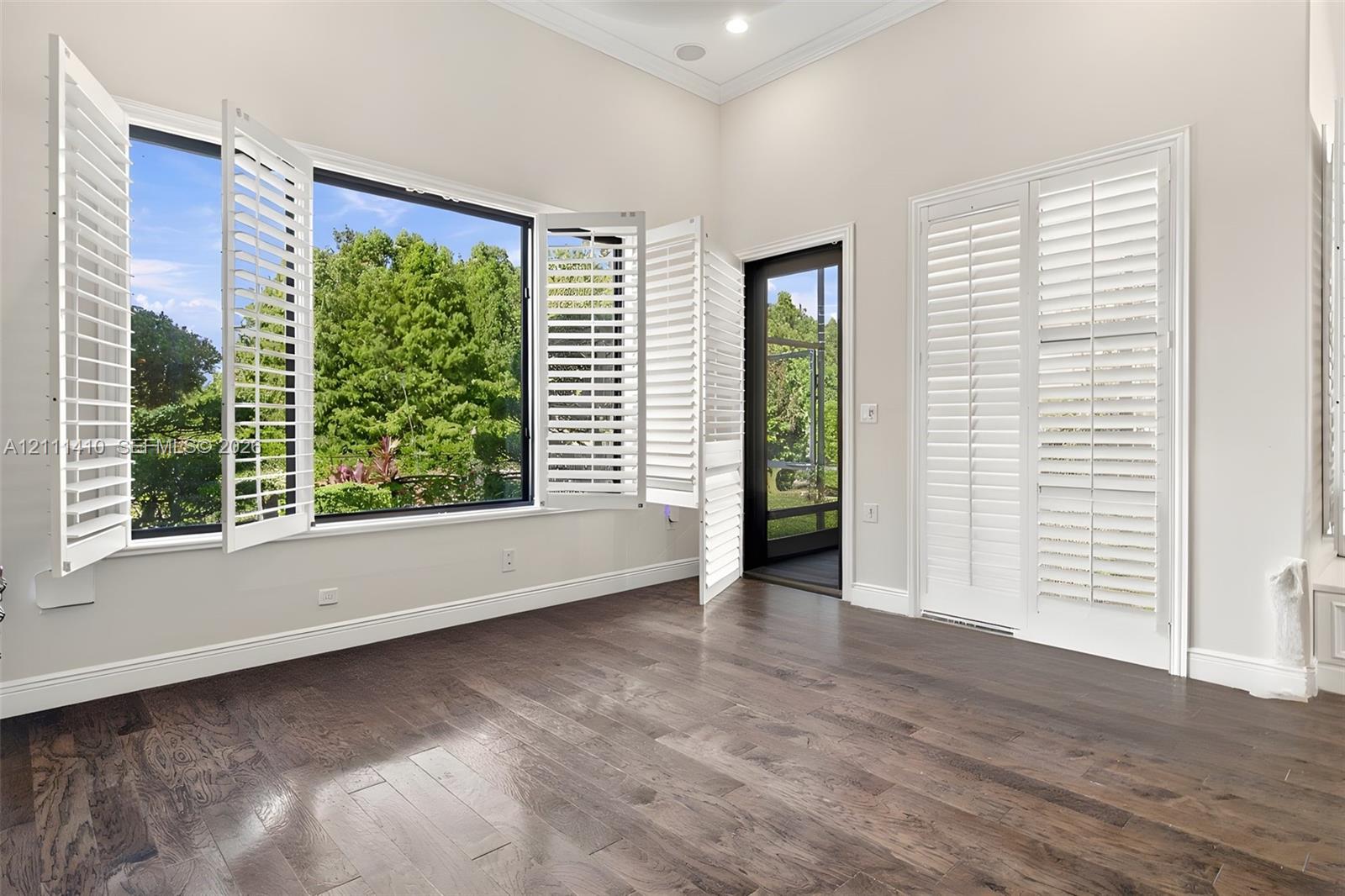 Wood-finish flooring, white plantation shutters, vaulted ceilings, and a framed glass door with screen panel Wood-finish flooring, white plantation shutters, vaulted ceilings, and a framed glass door with screen panel
