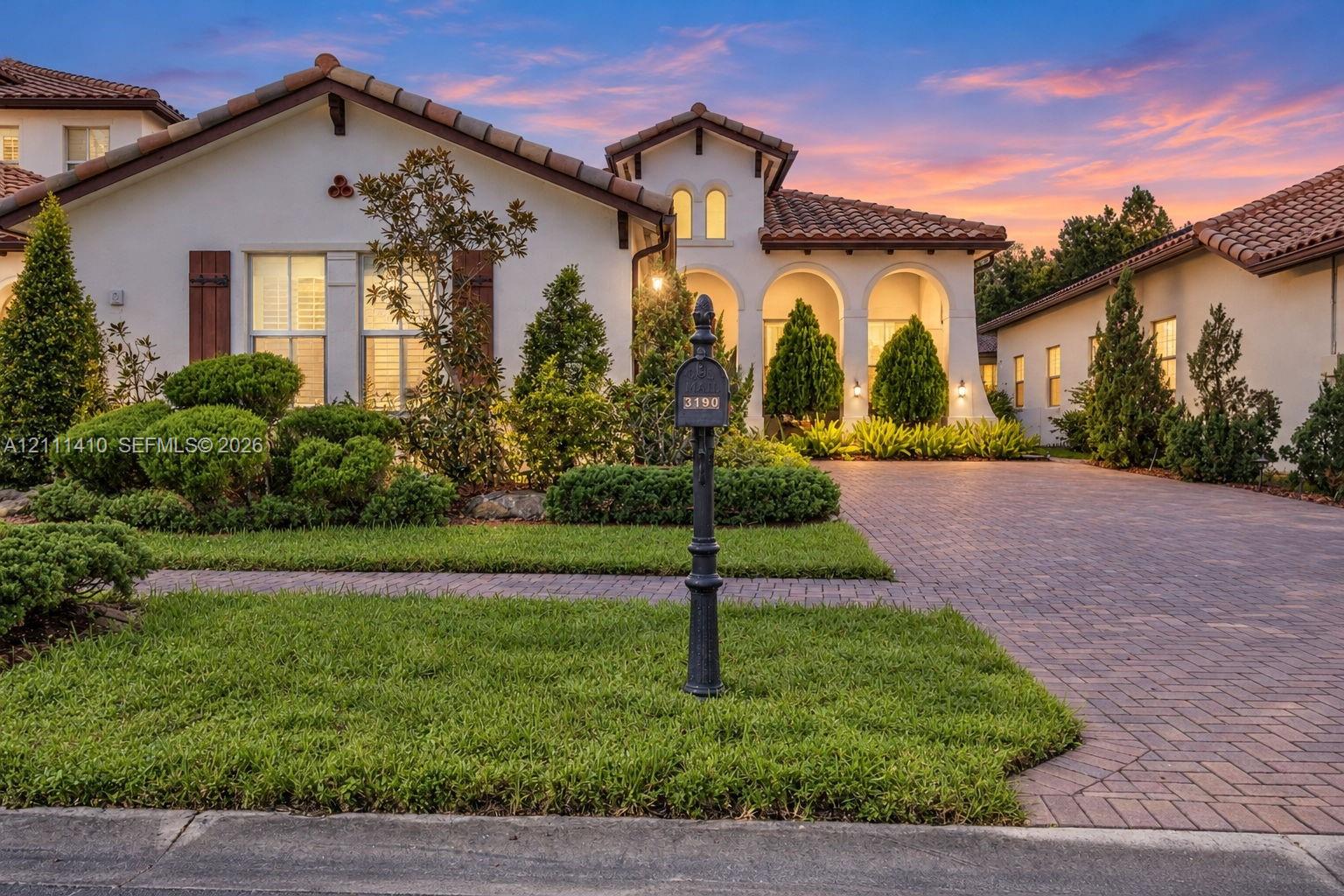 Stucco exterior featuring arched entryways, a terracotta-style tile roof, wood shutter accents, and a paver driveway Stucco exterior featuring arched entryways, a terracotta-style tile roof, wood shutter accents, and a paver driveway