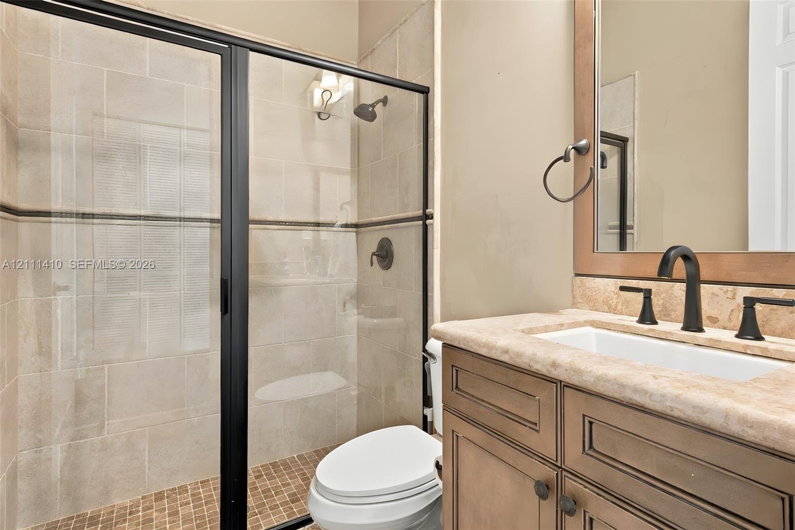 Shower with glass enclosure and black frame, vanity featuring a stone countertop and rectangular undermount sink, dark-finished hardware, and tile wall surround