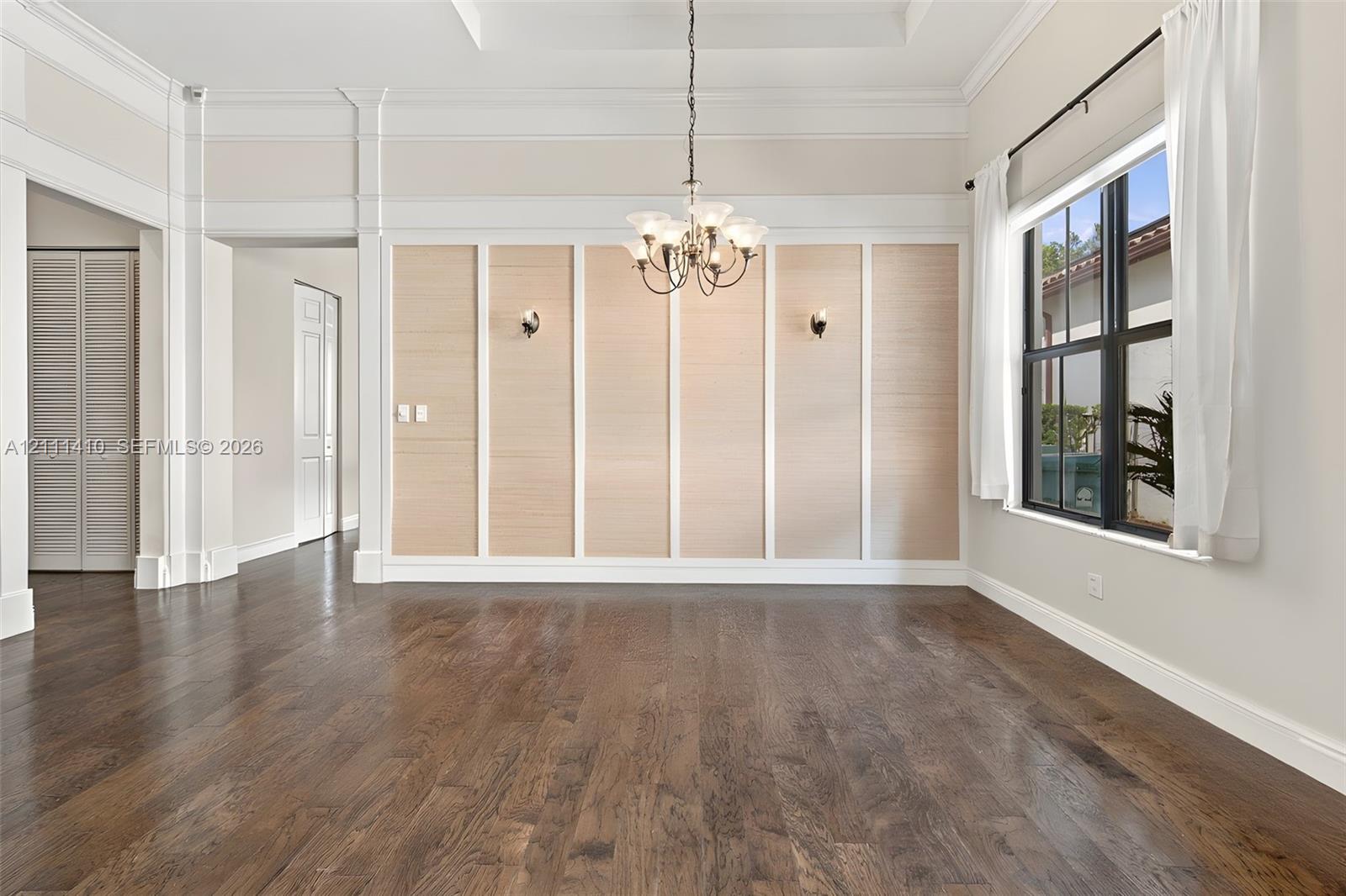 Interior space featuring wood-finish flooring, tray ceiling with crown molding, paneled accent wall, and multi-arm chandelier