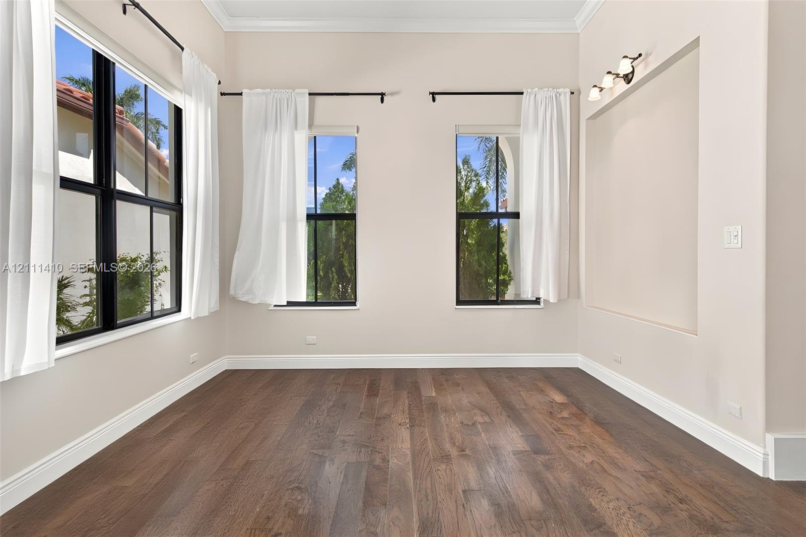 Room featuring dark wood-finish flooring, high ceilings with crown molding, black-framed windows, and a built-in recessed display niche with integrated accent lighting