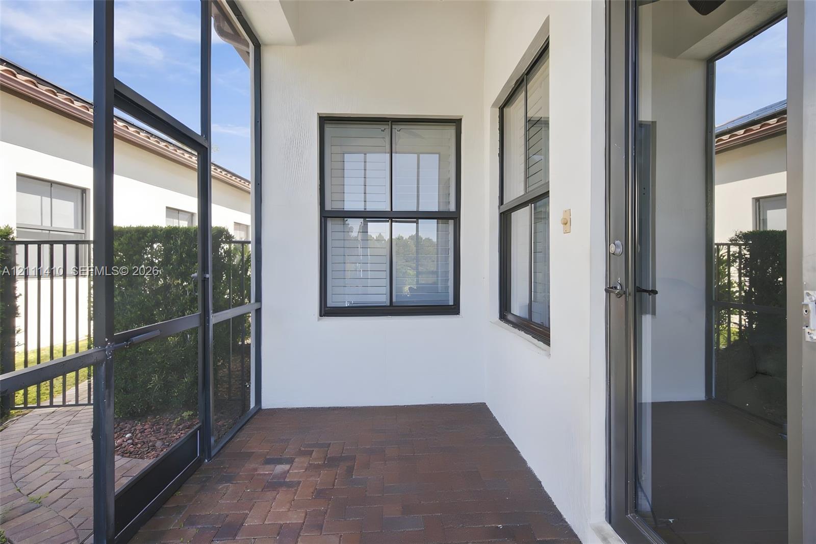Screened-in patio featuring brick-paver flooring, dark-framed window casing, and aluminum screen enclosures
