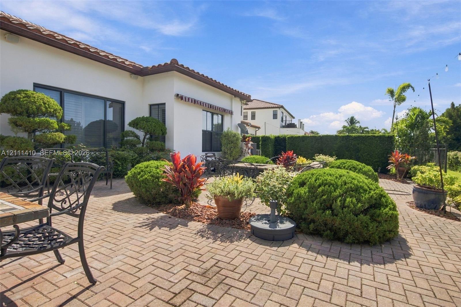 Spacious brick-paver patio featuring a herringbone pattern, exterior stucco finish, and manicured shrubbery
