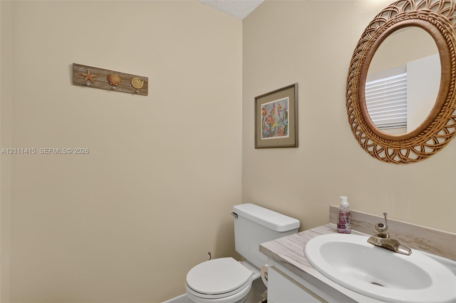 Neutral-toned powder room featuring a vanity with a white integrated oval sink, stone-finish laminate countertop, and a classic dual-handle faucet