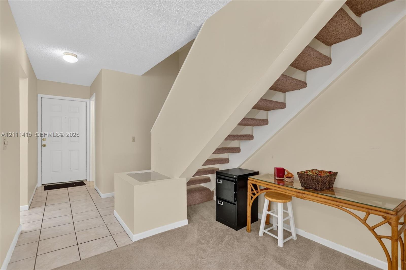 Foyer featuring neutral-toned tile flooring, carpeted staircase with enclosed structural balustrade, and a recessed ceiling light fixture