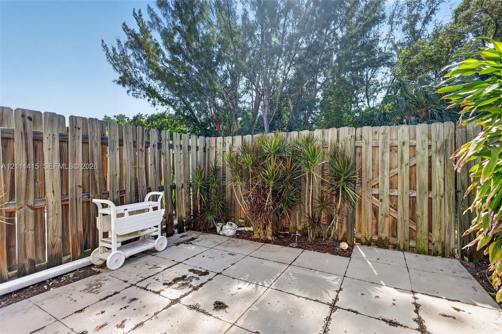 Rear patio featuring concrete pavers, enclosed by a vertical wood-board fence with an integrated gate and perimeter landscaping
