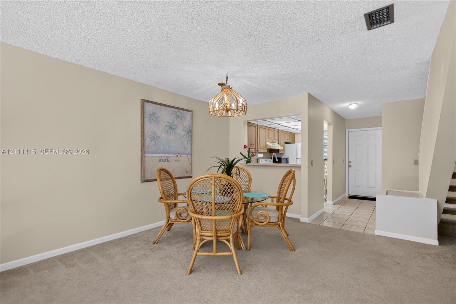 Dining area featuring a decorative pendant light fixture, pass-through opening to the kitchen, neutral wall tones, and carpeted flooring