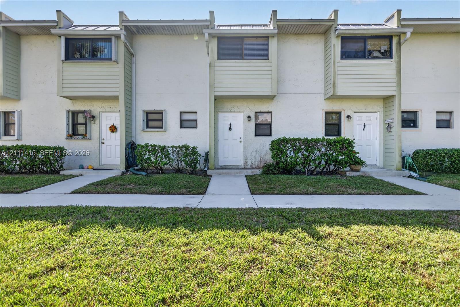 Multi-story exterior featuring light-toned stucco, horizontal siding accents, metal roof detailing, and concrete pathways