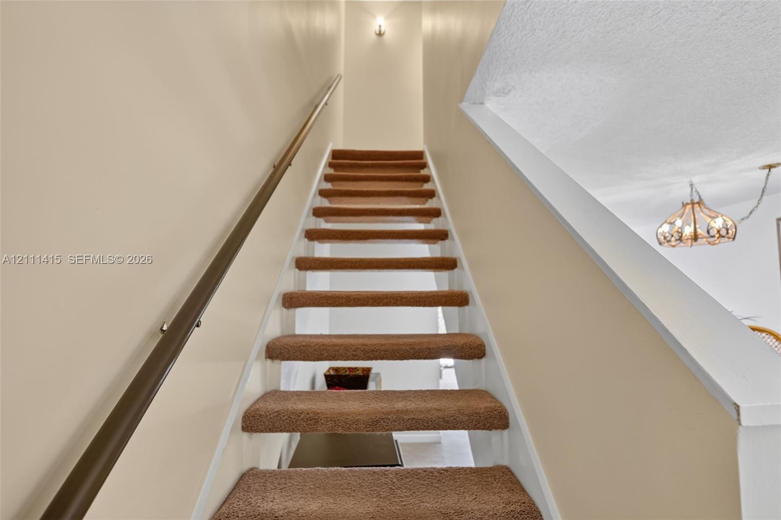 Staircase featuring wall-to-wall carpeted treads, a solid wood handrail with metallic mounting hardware, and a semi-flush mount ceiling light fixture