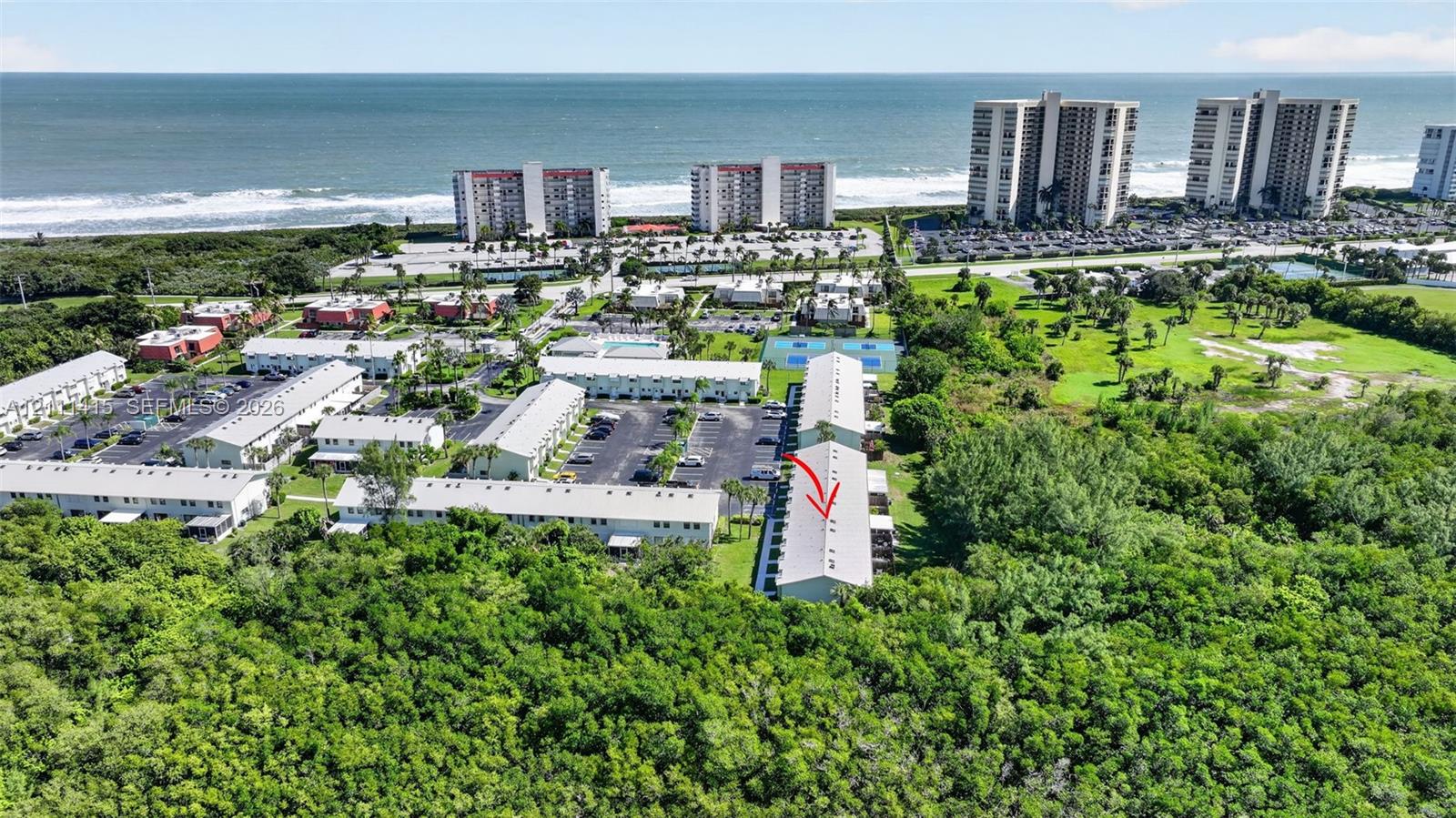 Aerial perspective of multi-unit residential complex featuring proximity to the coastline, surface parking areas, and tennis courts