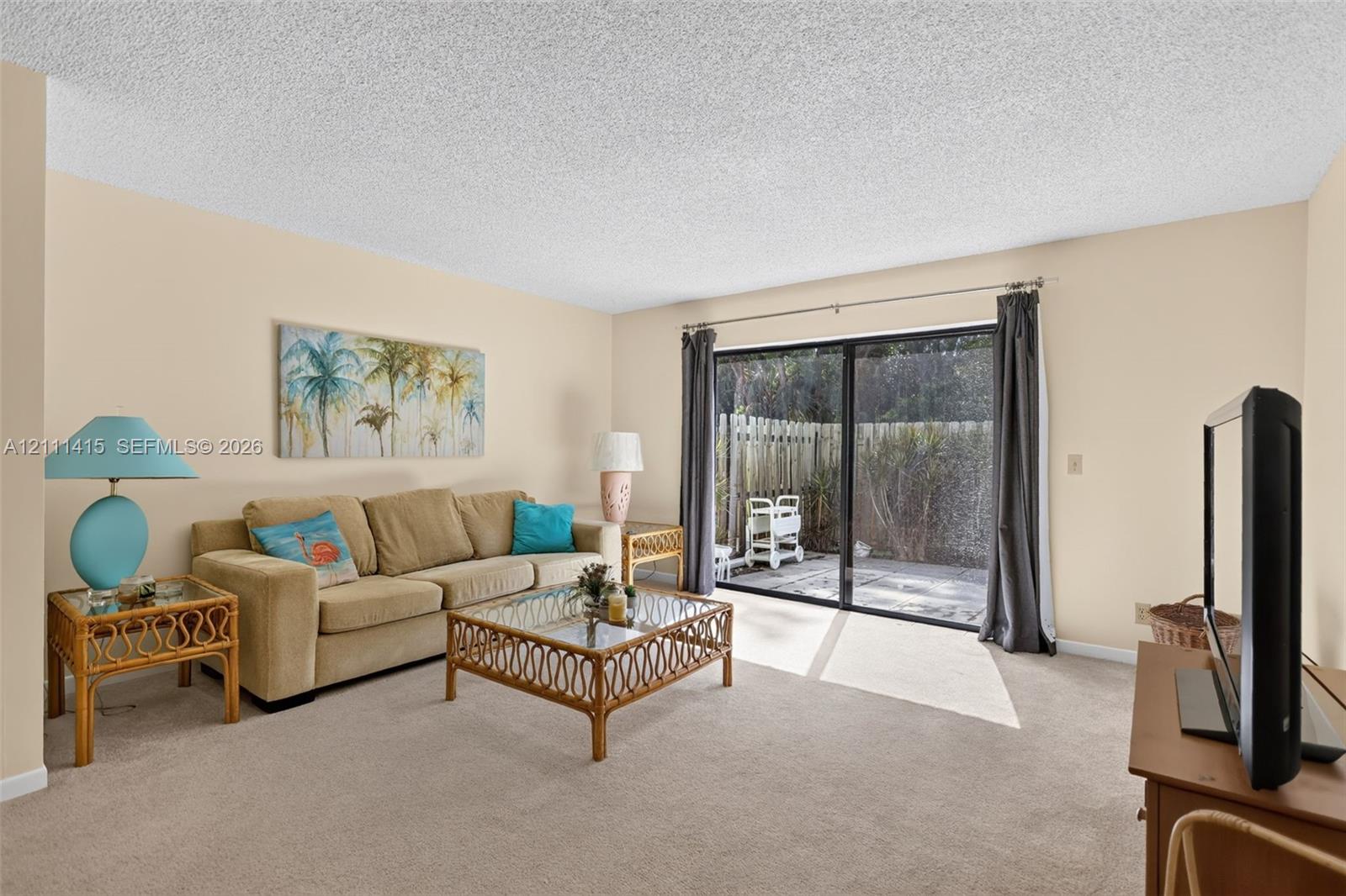 Living area featuring neutral wall paint, textured ceiling, carpeted flooring, and a large sliding glass door providing external access