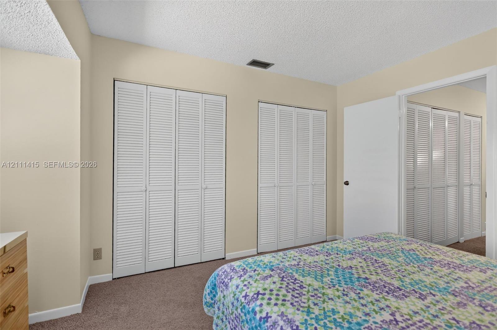 Room featuring neutral wall tones, textile flooring, and multiple sets of white louvered-style closet doors