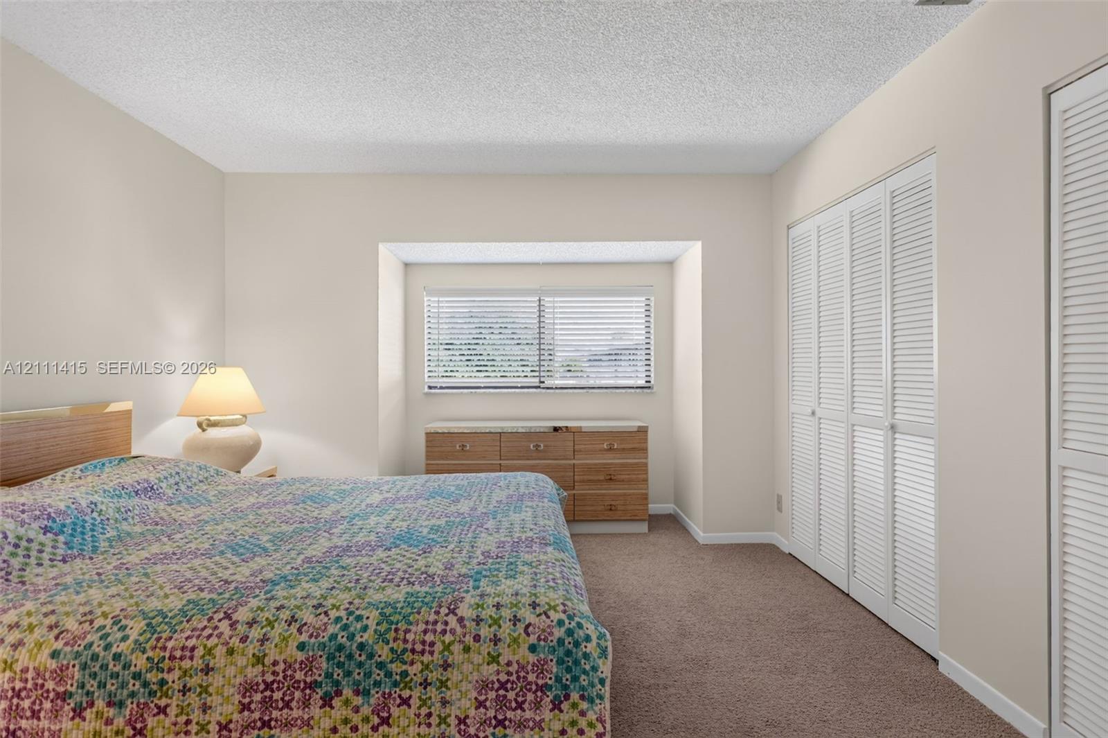 Recessed window nook featuring a horizontal window with blinds, carpeted flooring, and floor-to-ceiling closets with louvered doors