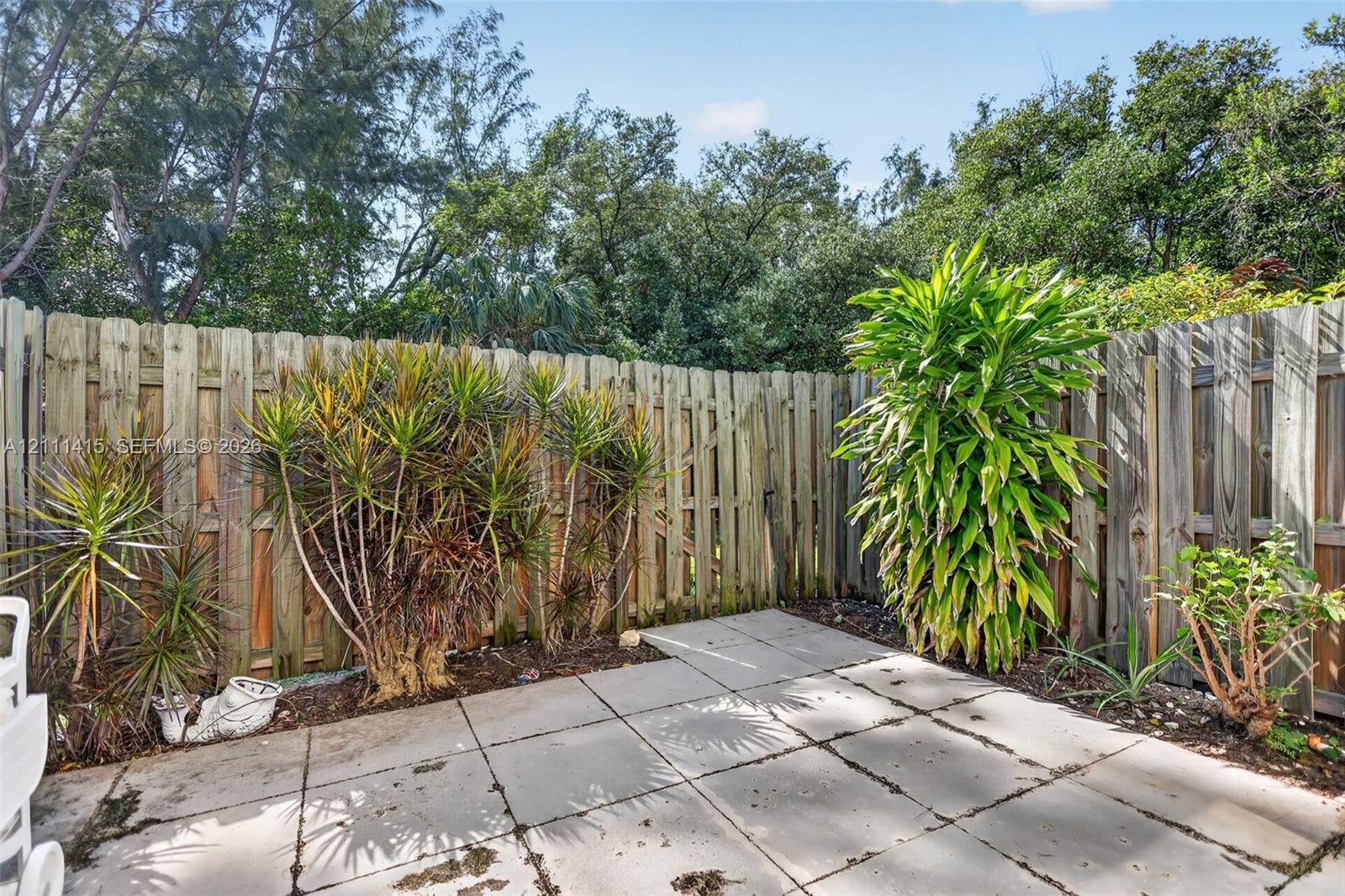 Rear patio featuring concrete pavers, wood privacy fencing, and mature landscaping