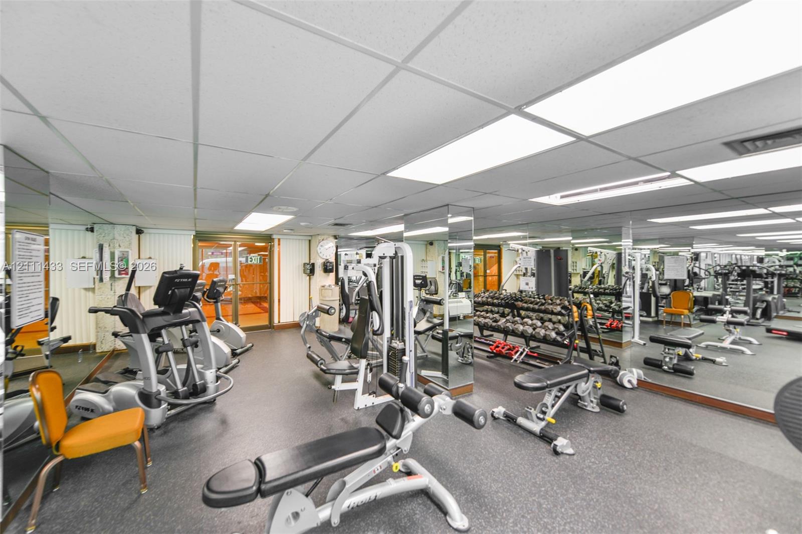 Fitness facility featuring full-wall mirrors, suspended acoustic ceiling tiles, and recessed fluorescent lighting
