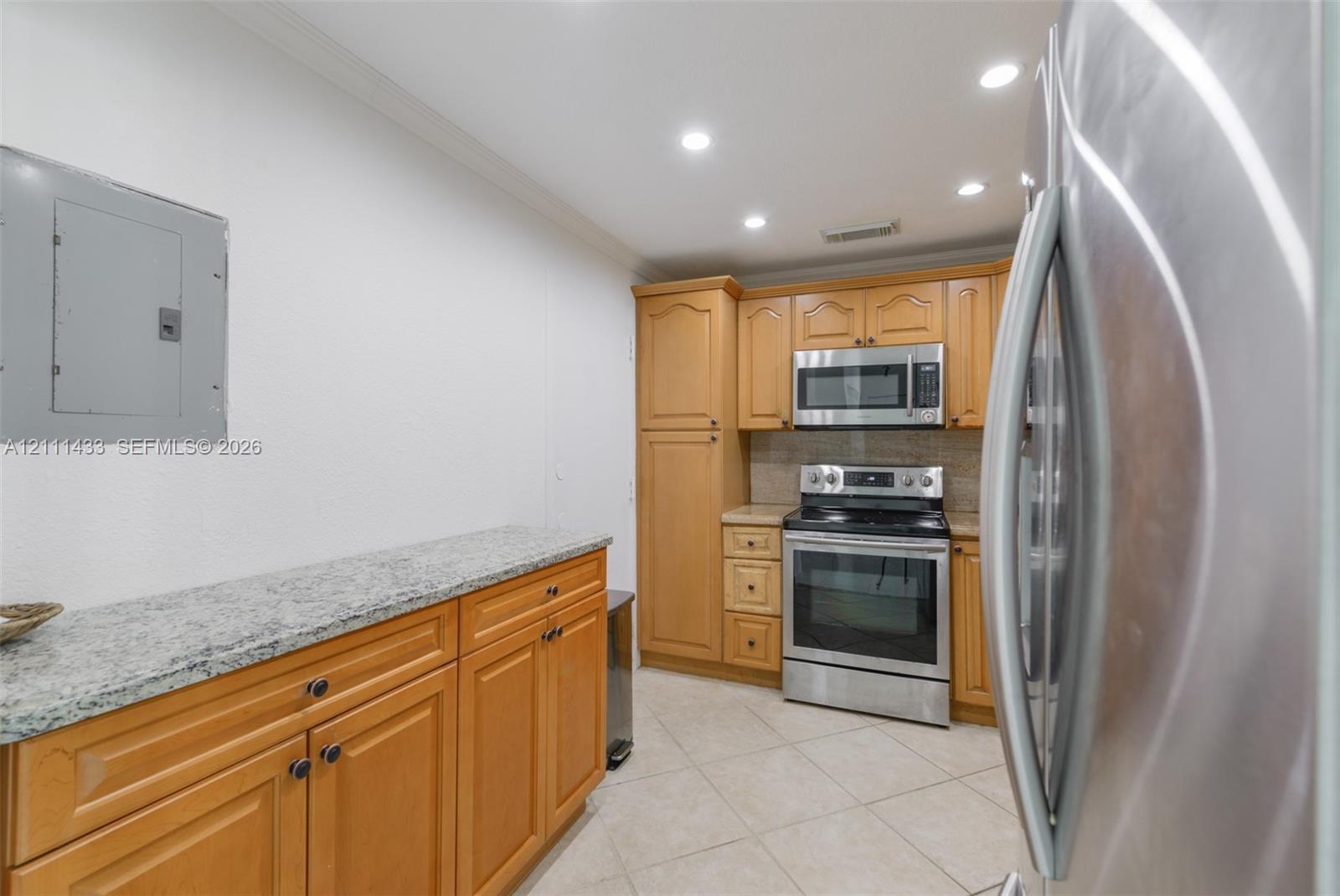 Kitchen featuring natural wood cabinetry, stone countertops, stainless steel appliances, recessed lighting, and tile flooring