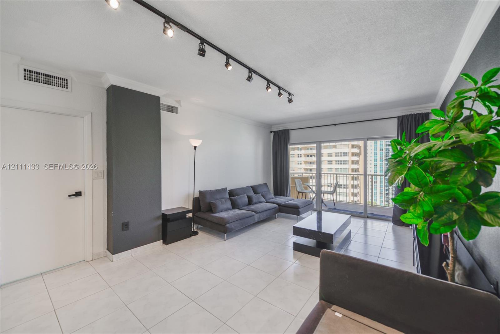Interior space featuring large-format tile flooring, adjustable track lighting, high-contrast charcoal accent walls, and sliding glass doors with balcony access