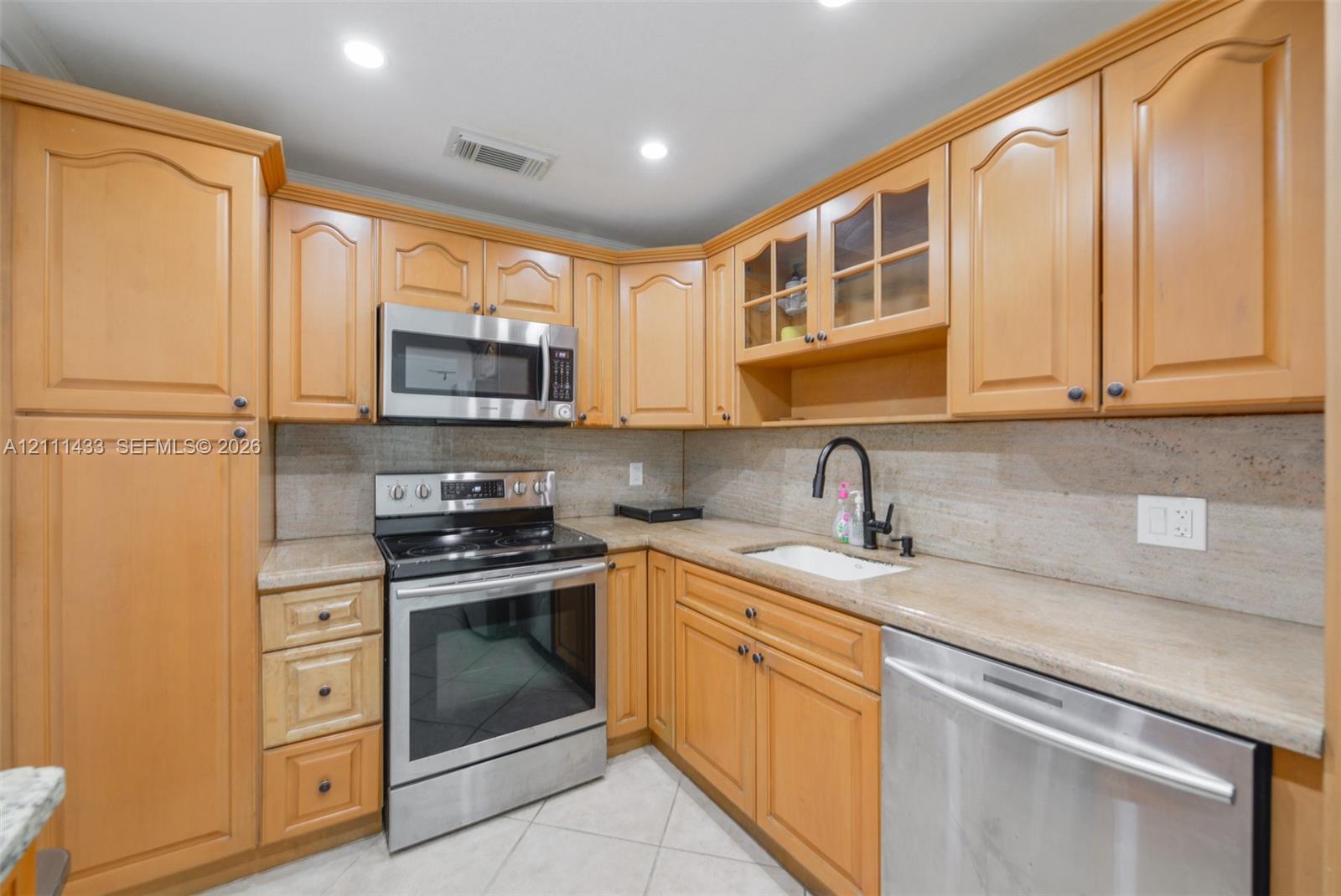 Kitchen featuring wood cabinetry, stone-finish countertops, stainless steel appliances, glass-front upper cabinet doors, and matte black plumbing fixtures