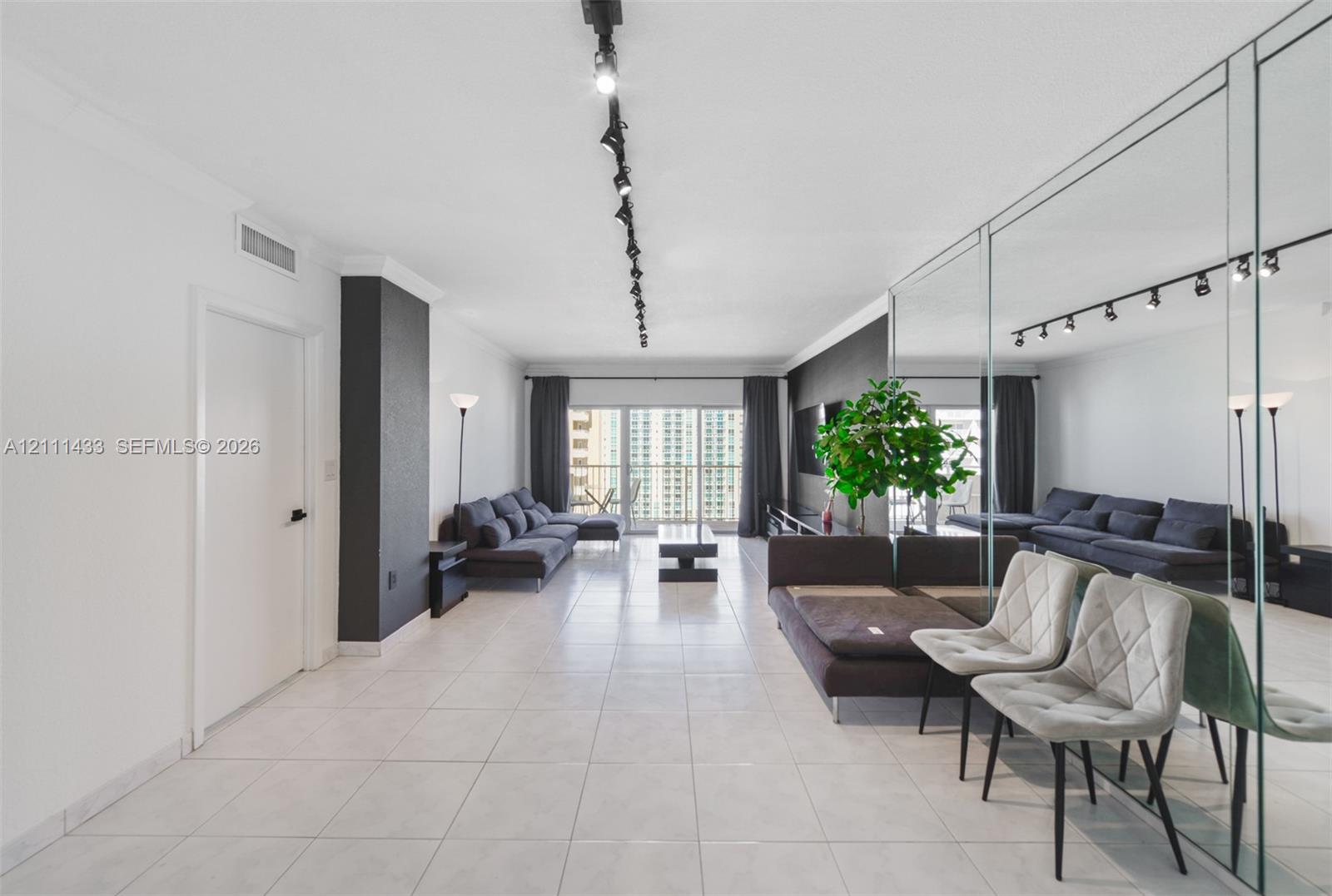 Living area featuring large-format tile flooring, a floor-to-ceiling mirrored wall, adjustable track lighting, and sliding glass doors with access to an exterior balcony