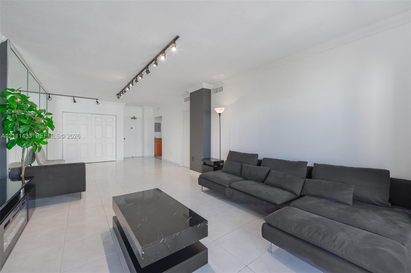 Open-concept living space featuring large-format tile flooring, a mirrored wall accent, a dark-toned structural pillar, and adjustable multi-light track lighting