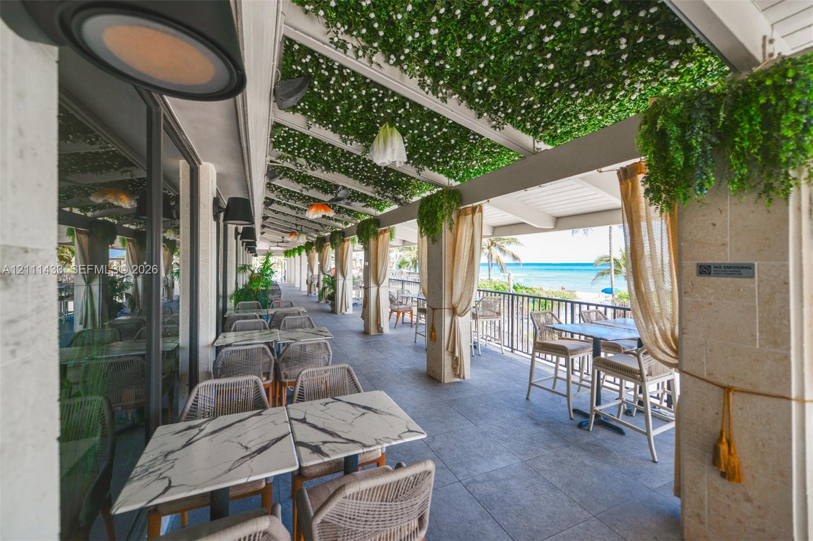 Covered outdoor terrace featuring a stone-clad pergola with integrated greenery, tile flooring, stone pillars, and direct ocean backdrop