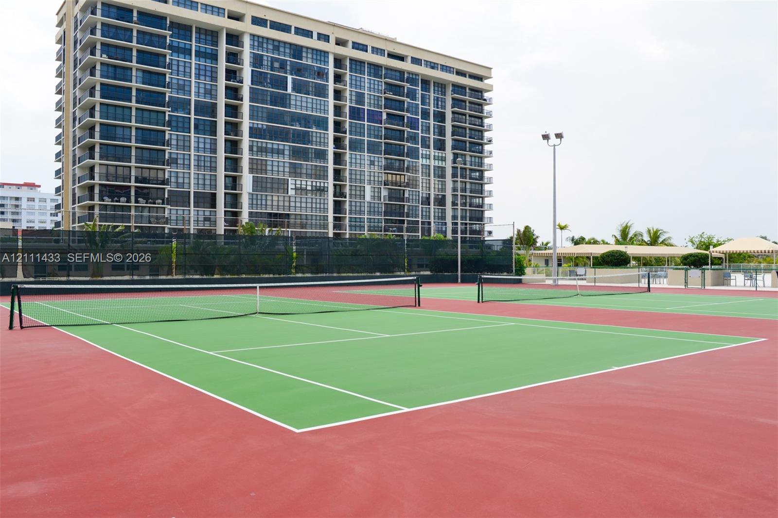 Two full-size tennis courts with high-visibility surfacing, chain-link perimeter fencing, and integrated lighting fixtures