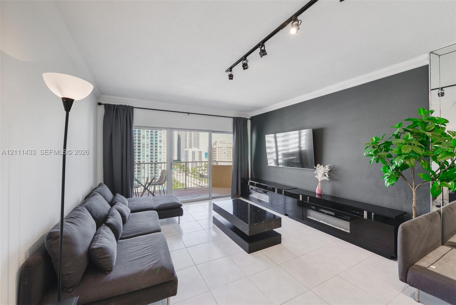 Living area featuring oversized ceramic tile flooring, a charcoal accent wall, integrated track lighting, and sliding glass doors with balcony access