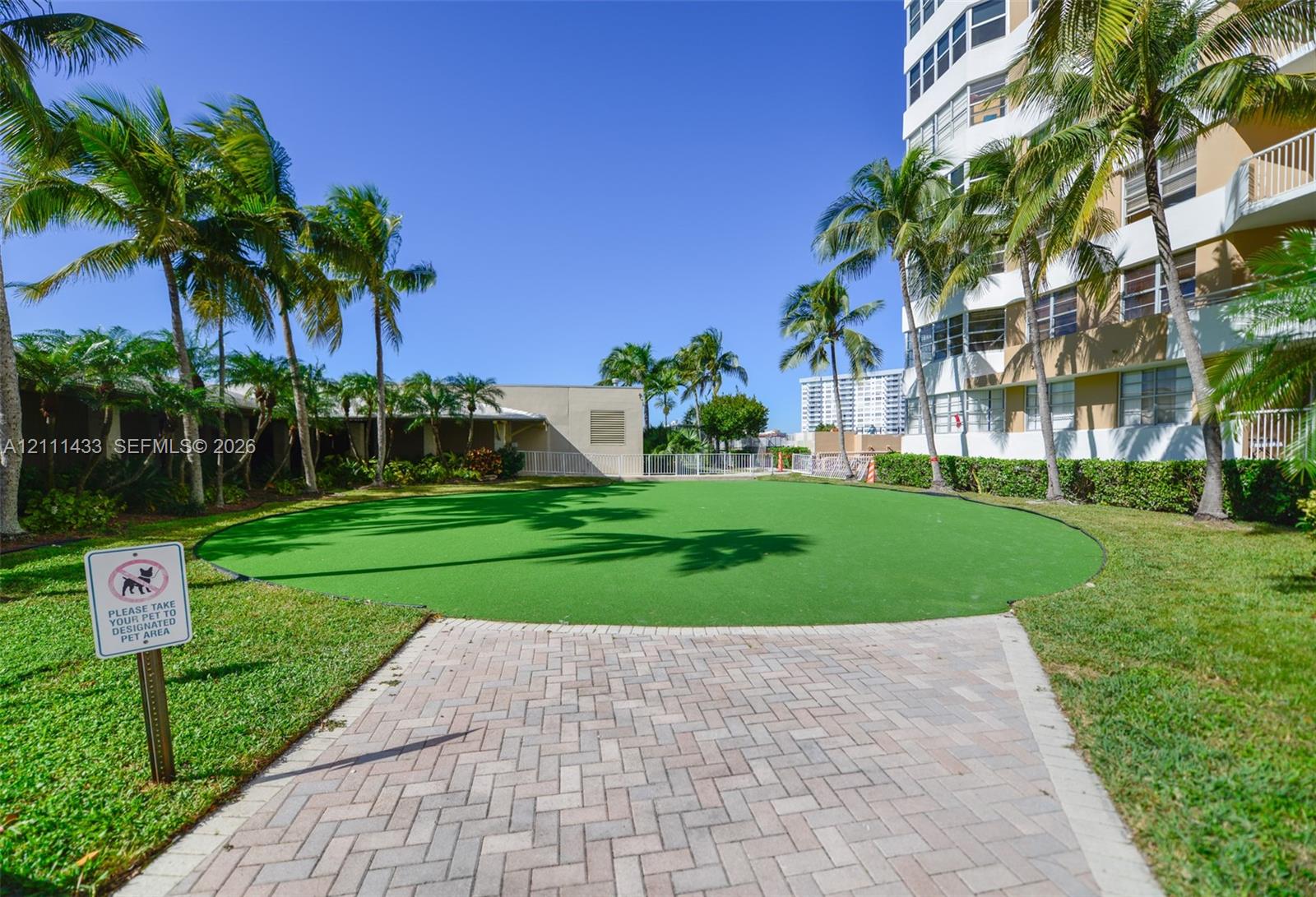 Manicured artificial turf lawn with paver walkway, mature palm trees, and perimeter landscaping