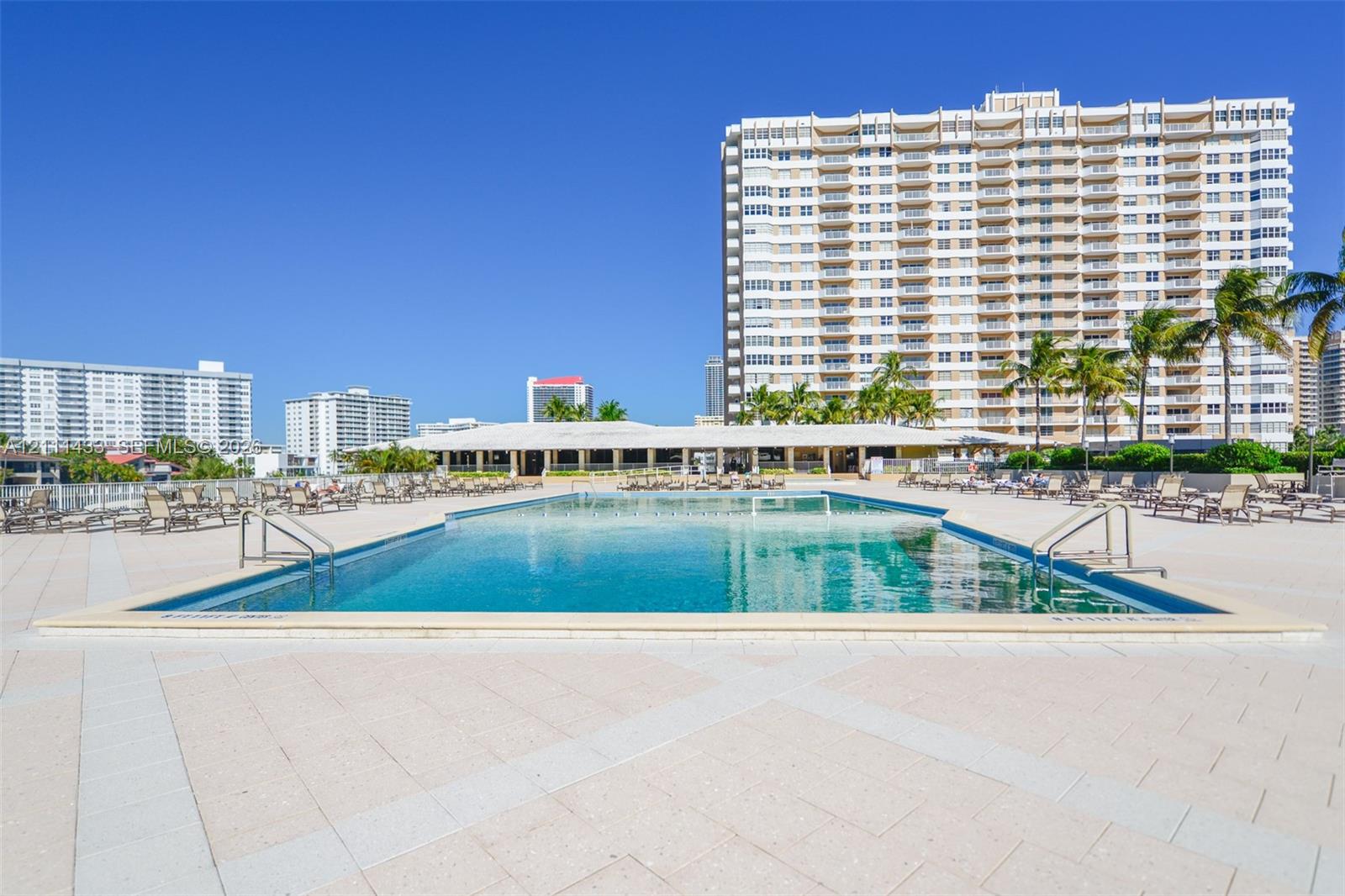 In-ground swimming pool featuring a concrete deck, metal handrails, and surrounding palm trees