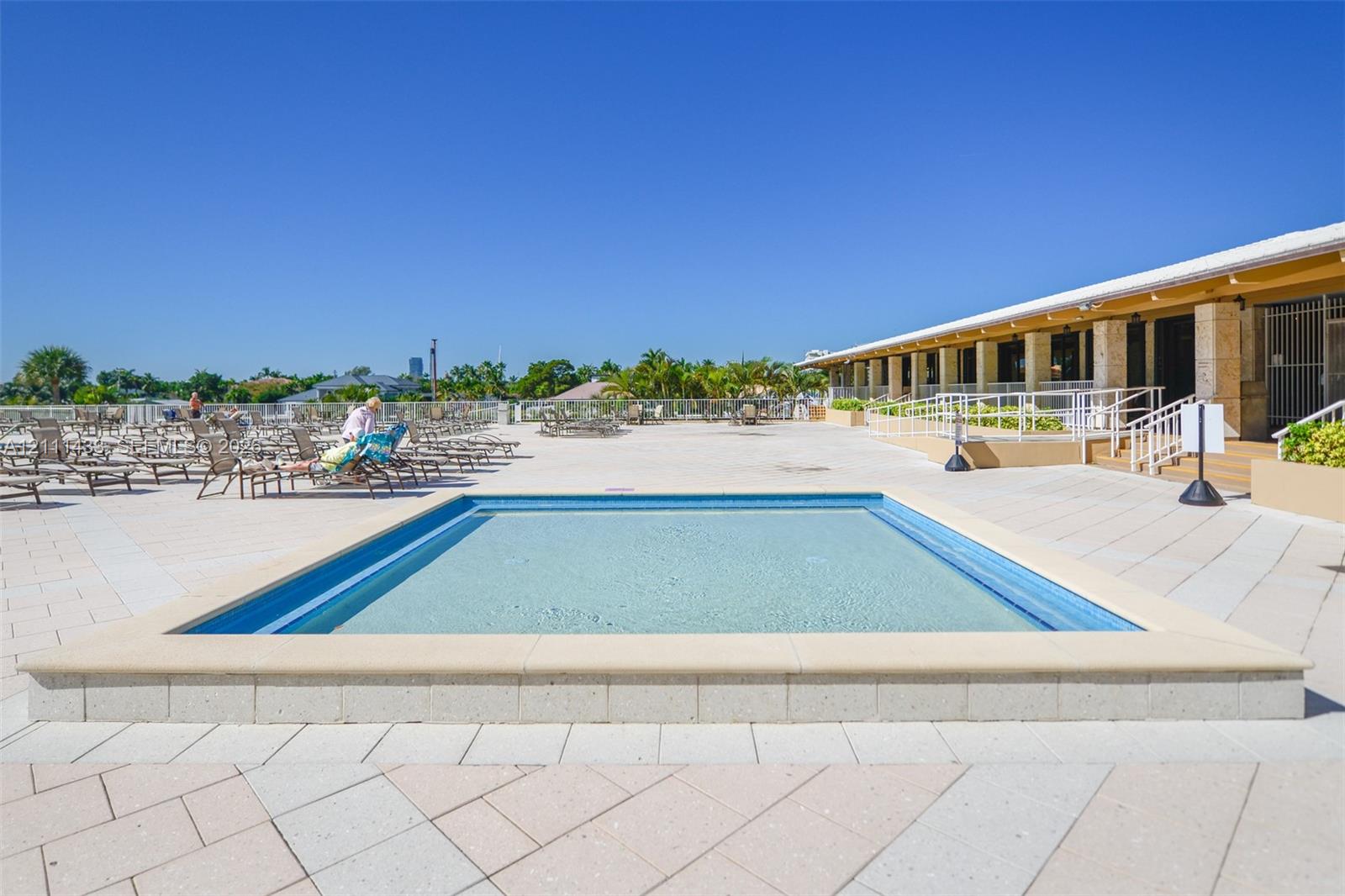 Expansive paved sun deck featuring an integrated swimming pool with a stone coping border and white metal railings