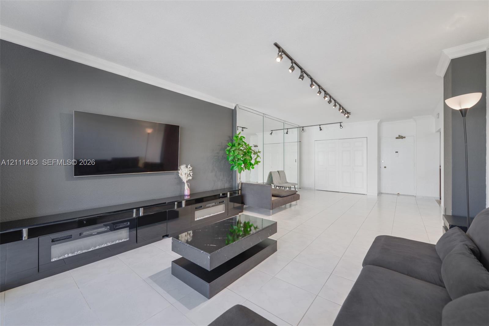 Living area featuring large-format white tile flooring, recessed track lighting, mirrored wall panels, and a matte-finish accent wall