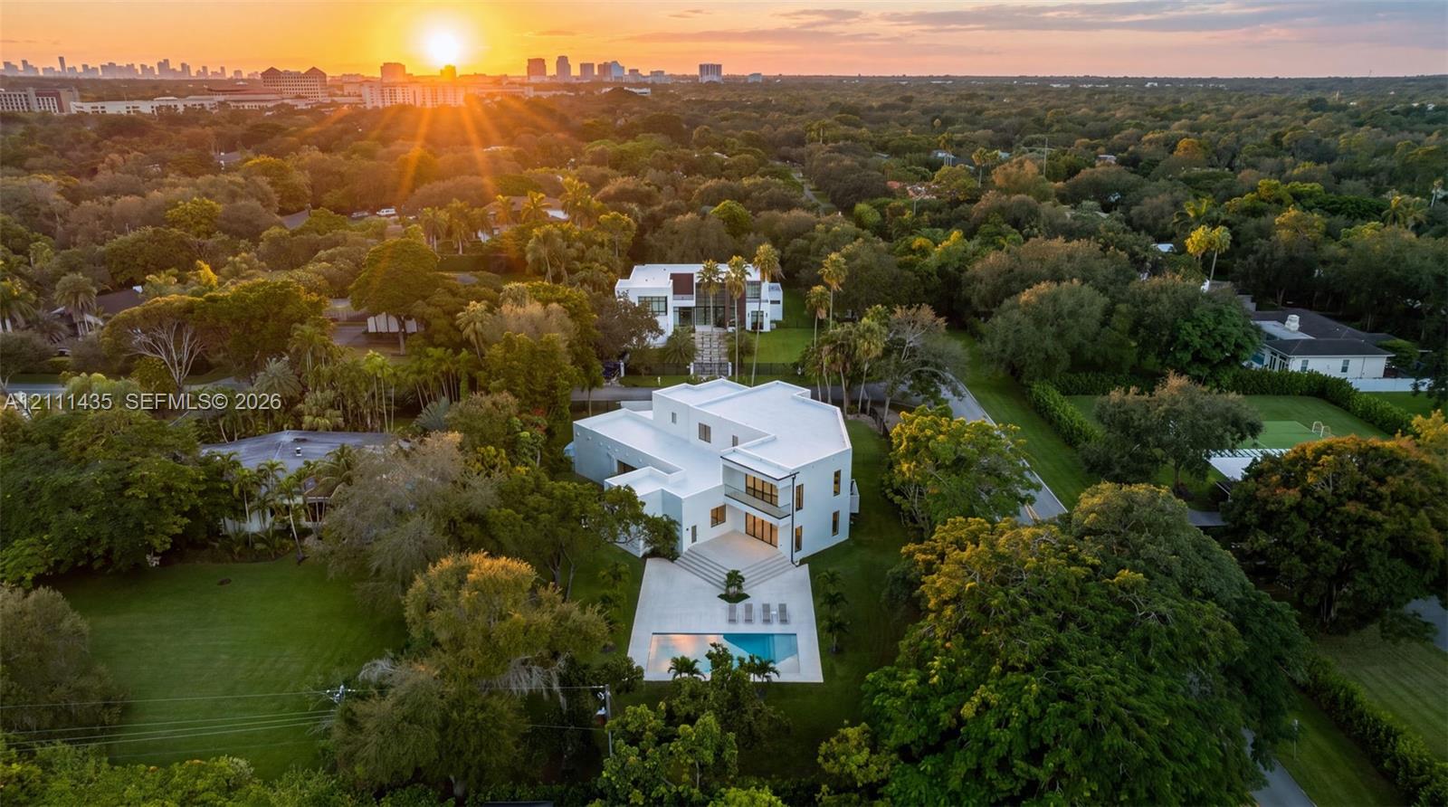 Modern architectural estate featuring a flat roofline, multi-level exterior, rear swimming pool, concrete patio, and landscaped grounds