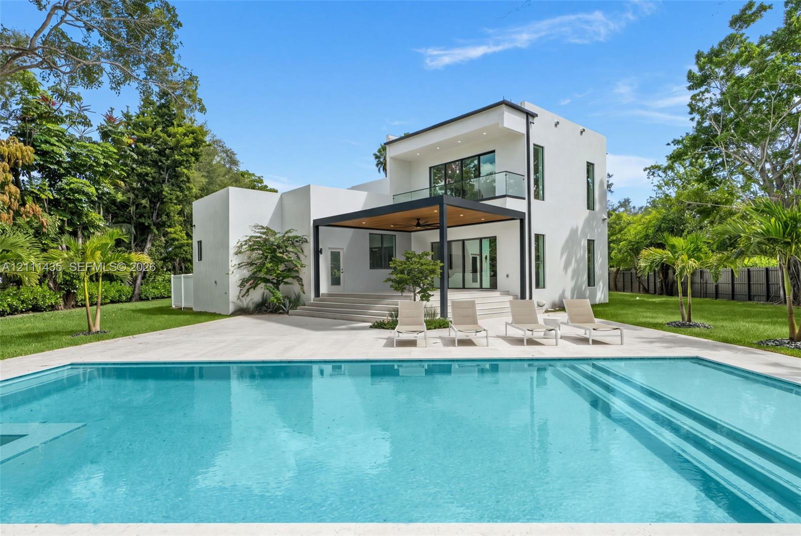 Modern two-story residence featuring a smooth stucco exterior, expansive concrete patio, built-in swimming pool with step entry, and a covered pavilion with recessed lighting