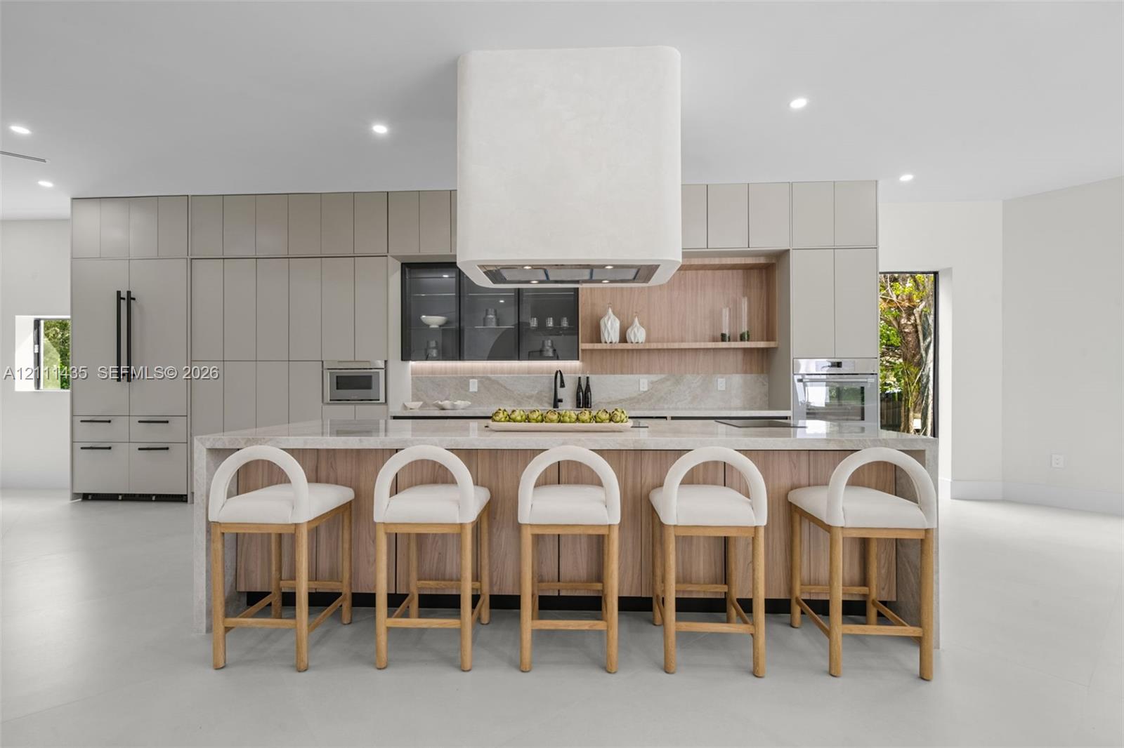 Kitchen featuring a waterfall-edge island, custom cabinetry, integrated high-end appliances, a stone-finish backsplash, and a floating range hood