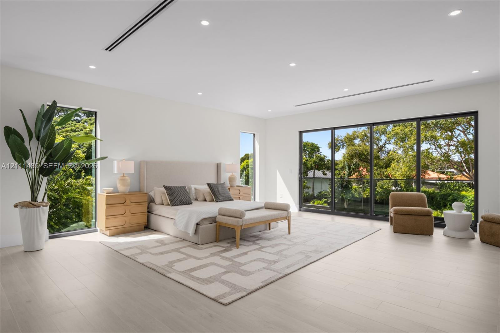 Spacious interior featuring light-toned wood-finish flooring, recessed lighting, full-height windows, and floor-to-ceiling sliding glass doors with dark metal frames
