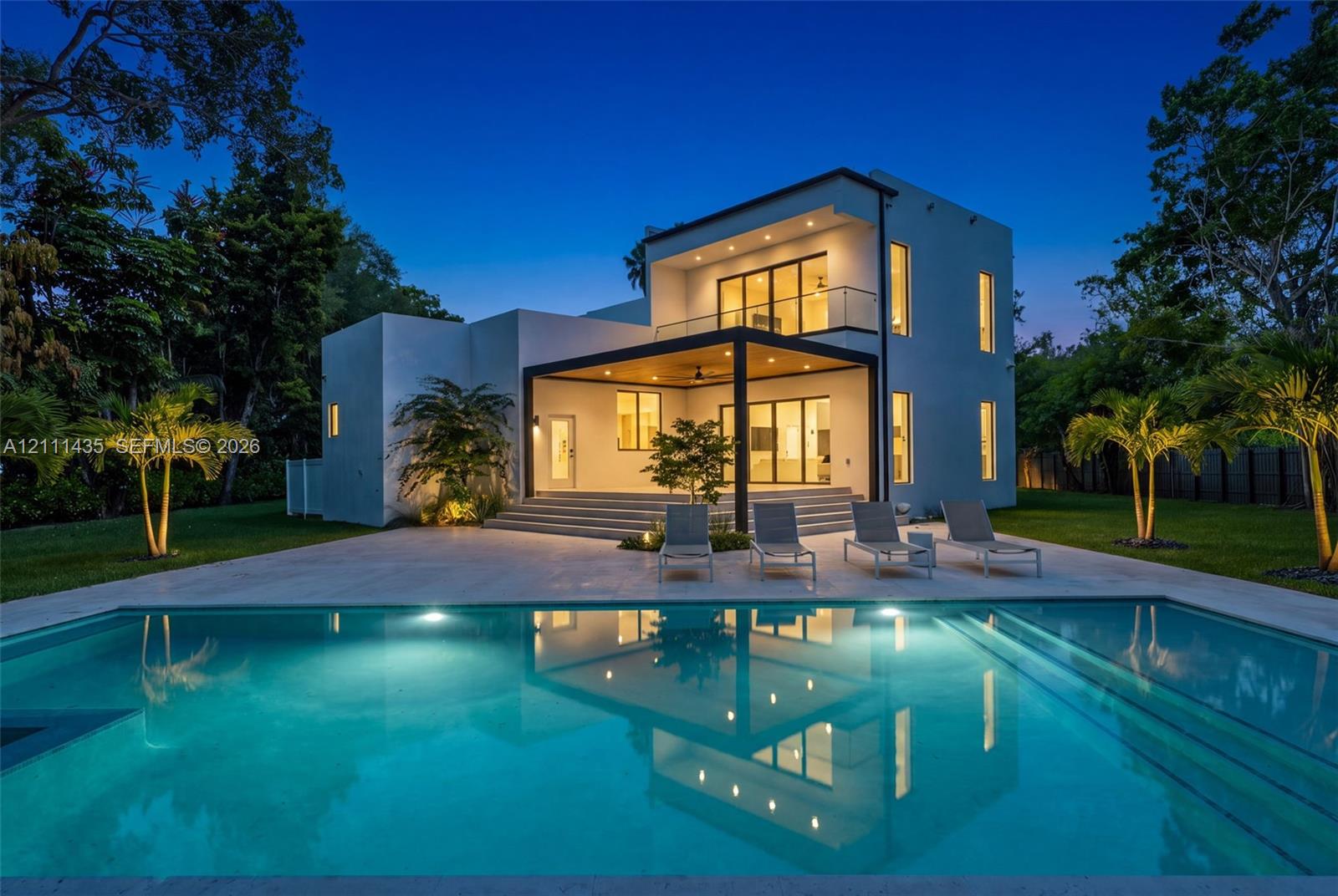 Modern two-story residence featuring a smooth stucco exterior, a covered patio with recessed lighting, a second-level balcony with a glass railing, and an inground swimming pool with stone decking