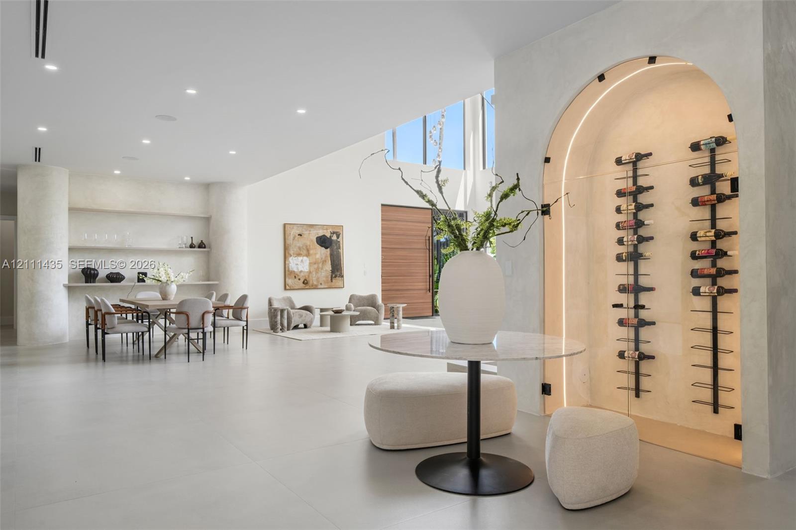 Arched, climate-controlled glass wine display with integrated accent lighting, built-in shelving, smooth plaster wall finishes, recessed ceiling lighting, and large-format tile flooring