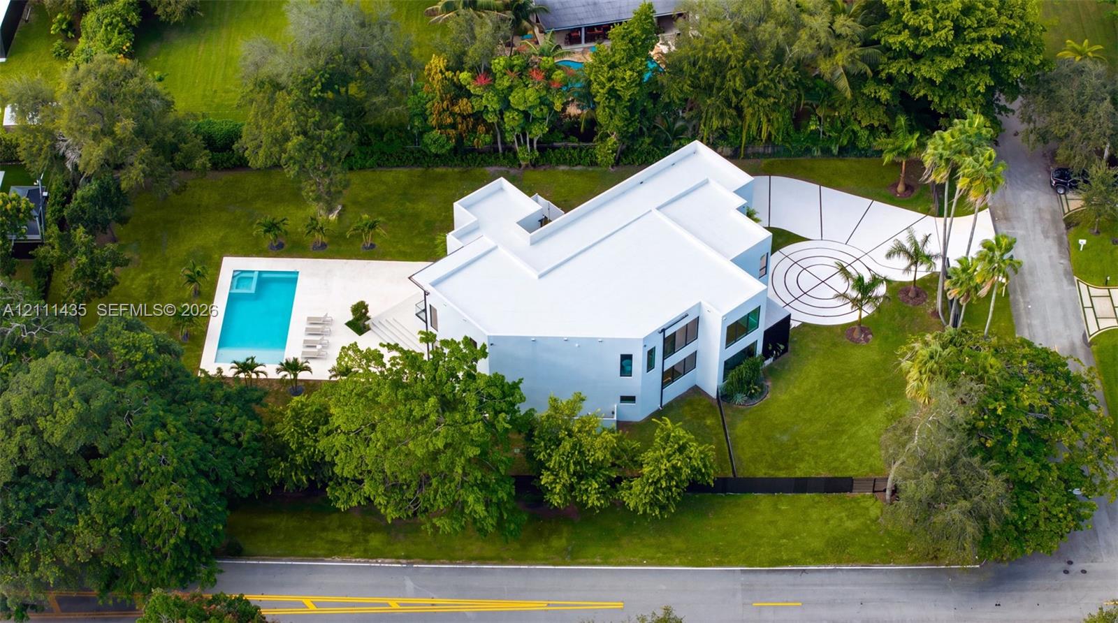 Modern multi-level estate featuring a flat-roof architectural design, a private swimming pool with an integrated spa, expansive lawn, and a decorative concrete driveway with geometric detailing