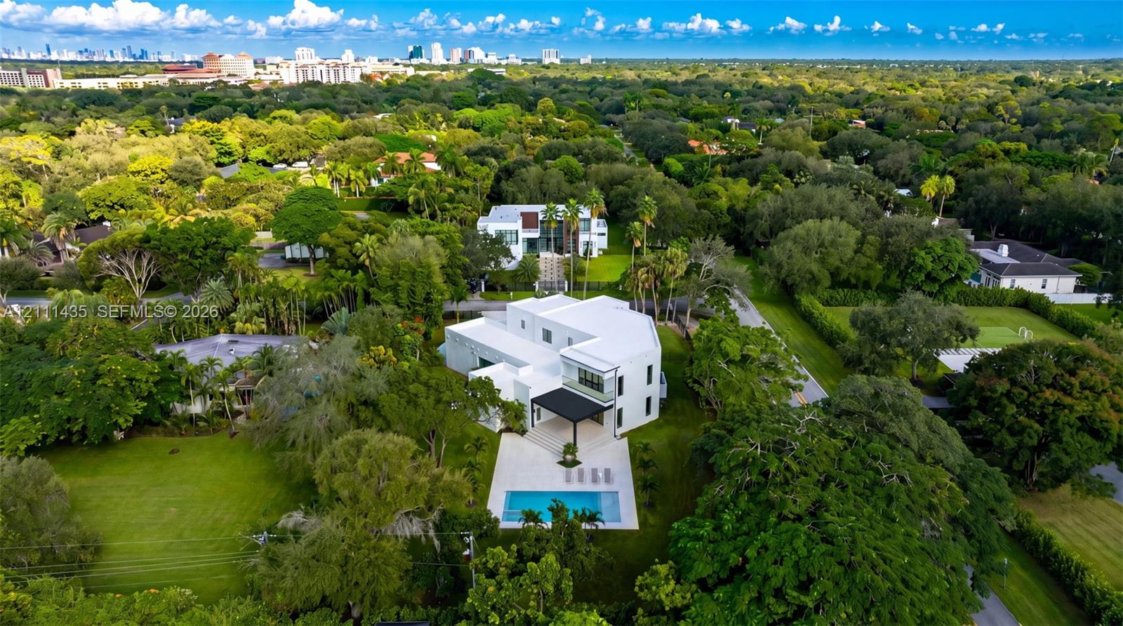 Multi-level modern residence featuring a white exterior, a covered rear patio, a swimming pool, and a manicured lawn set within a wooded lot