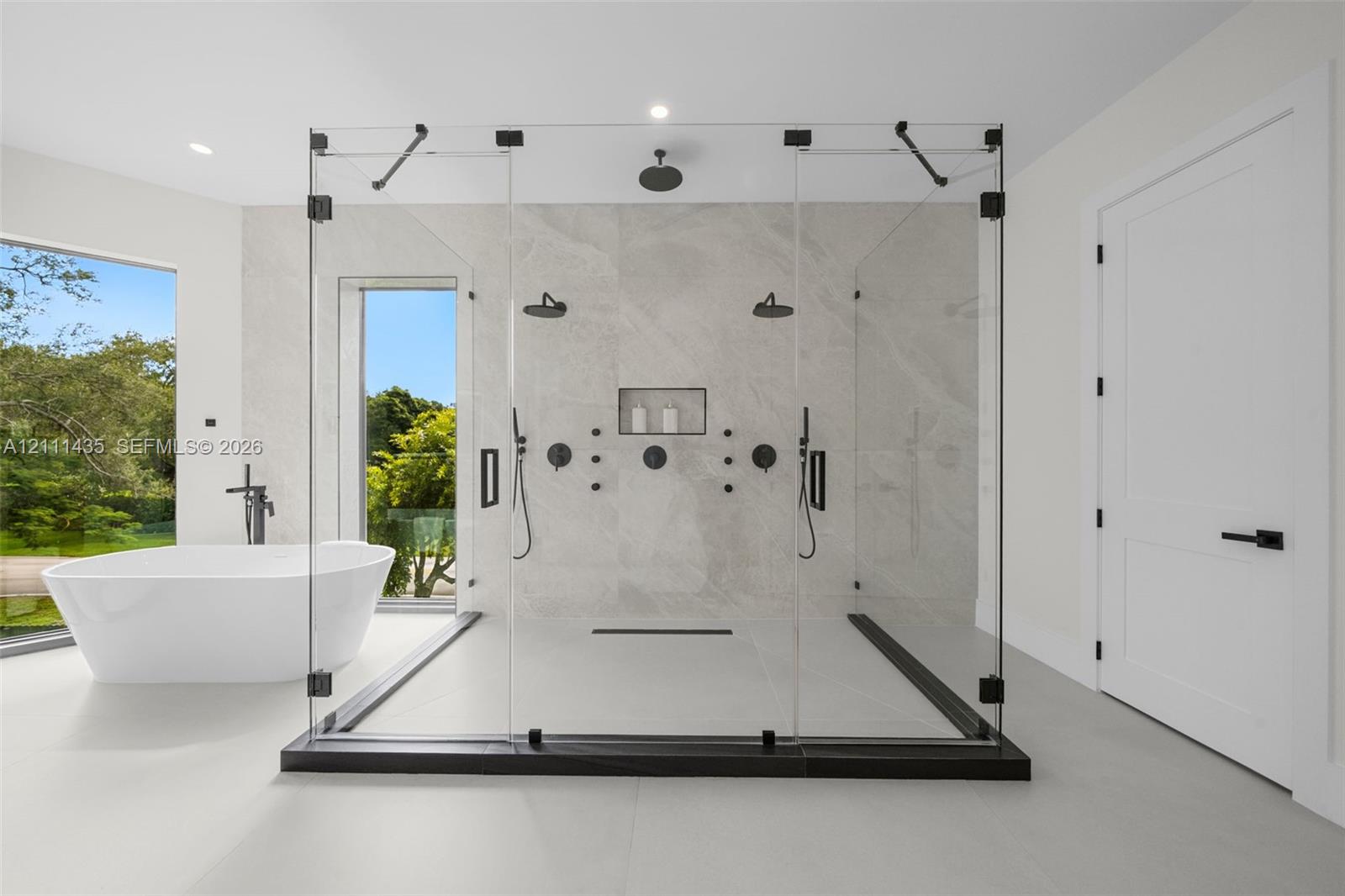 Walk-in glass-enclosed shower featuring dual shower heads, a built-in recessed niche, and stone-finish wall tile, paired with a freestanding soaking tub and matte black fixtures