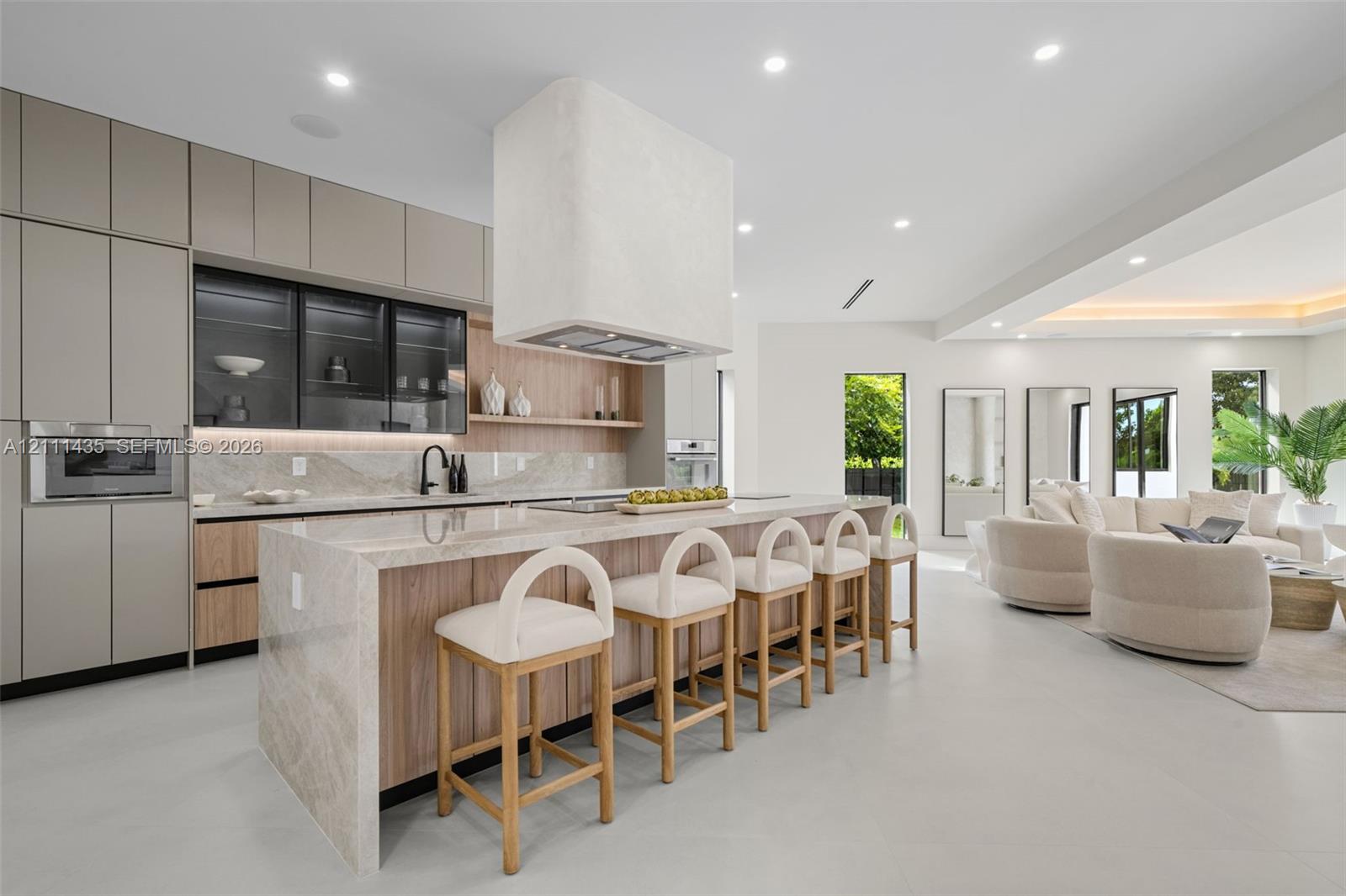 Modern kitchen featuring matte-finish cabinetry, a waterfall-edge stone island, integrated oven and microwave, recessed lighting, and a custom plaster range hood
