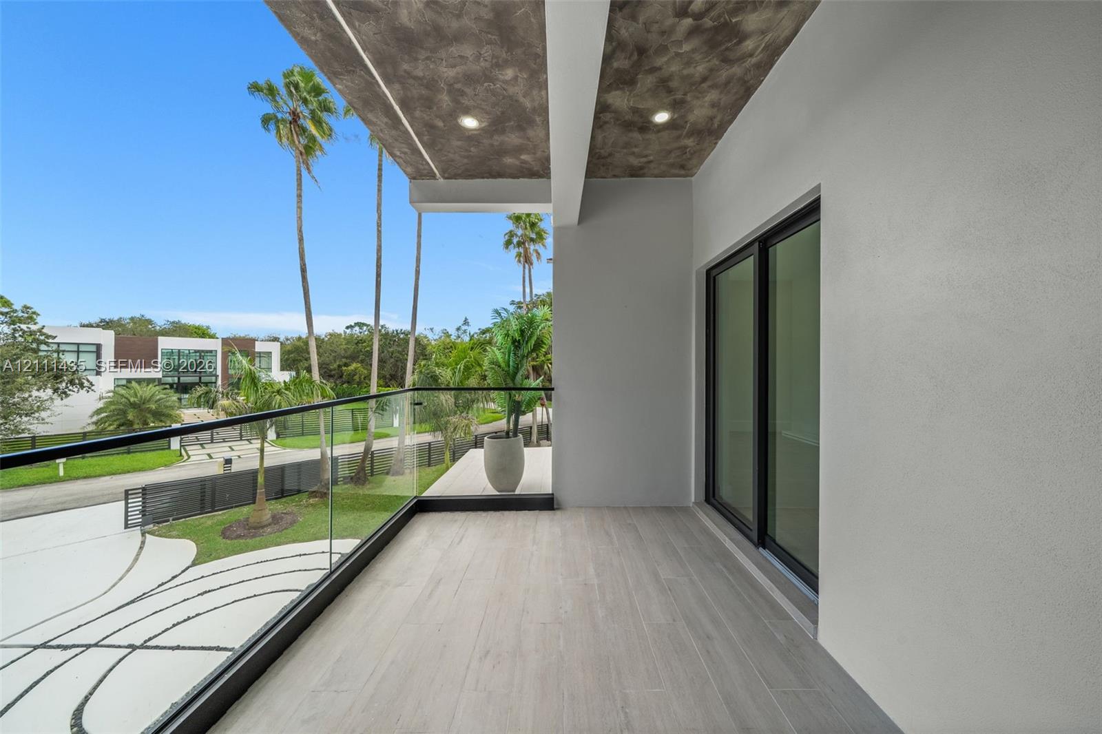 Covered balcony featuring wood-finish flooring, recessed lighting, concrete-texture ceiling finish, and a glass panel railing