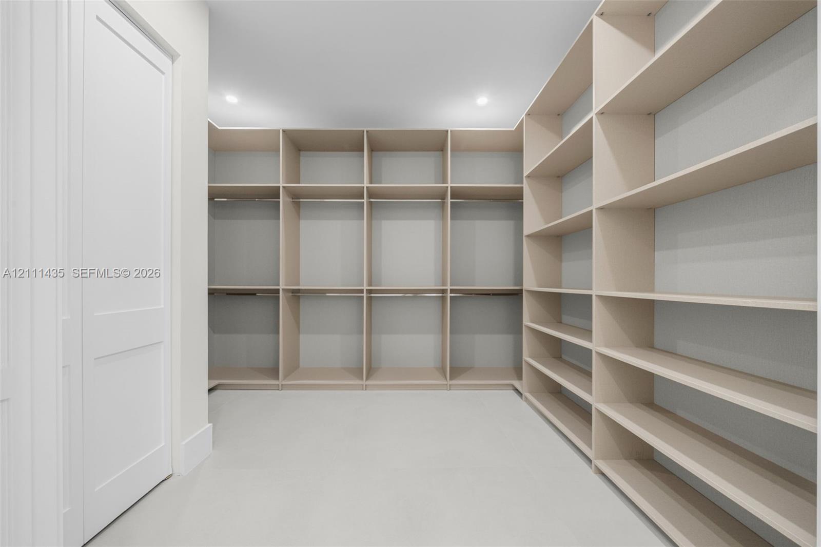 Custom walk-in storage area featuring extensive built-in shelving, integrated hanging rods, crisp white walls, and recessed lighting