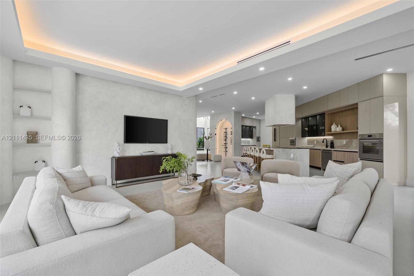 Open-concept interior featuring a recessed tray ceiling with integrated cove lighting, textured wall finish, built-in display shelving, and custom cabinetry with wood-tone accents