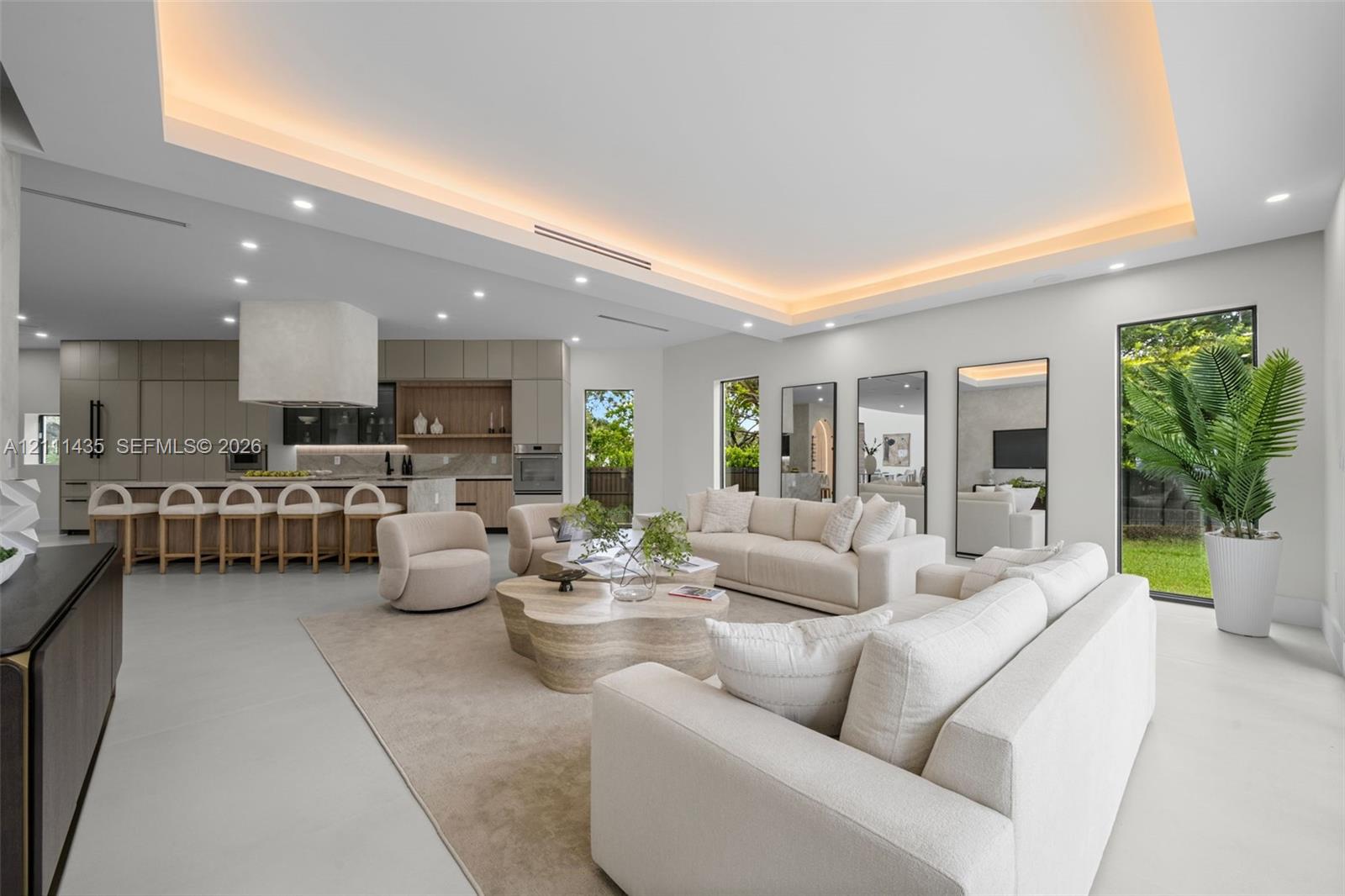 Open-concept interior featuring a recessed tray ceiling with integrated cove lighting, polished concrete flooring, built-in floor-to-ceiling cabinetry, and full-height windows