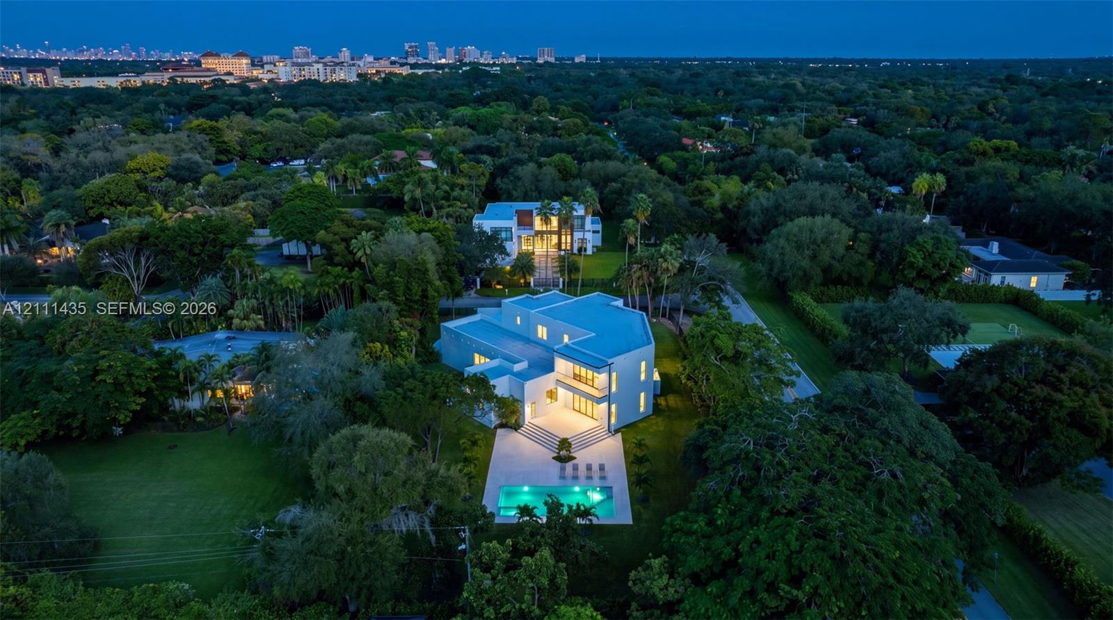 Aerial perspective featuring a multi-level contemporary residence, expansive manicured grounds, a rectangular swimming pool, and mature foliage