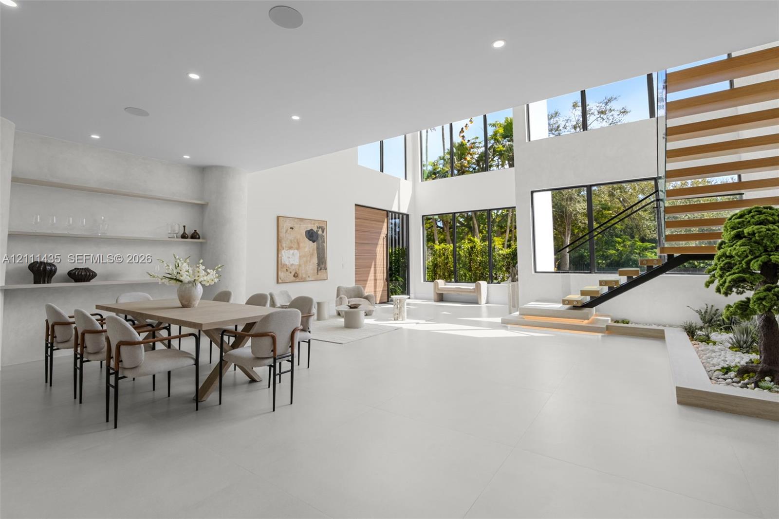 Double-height living area featuring large-format tile flooring, floor-to-ceiling windows, custom built-in recessed shelving, and a floating staircase with integrated lighting