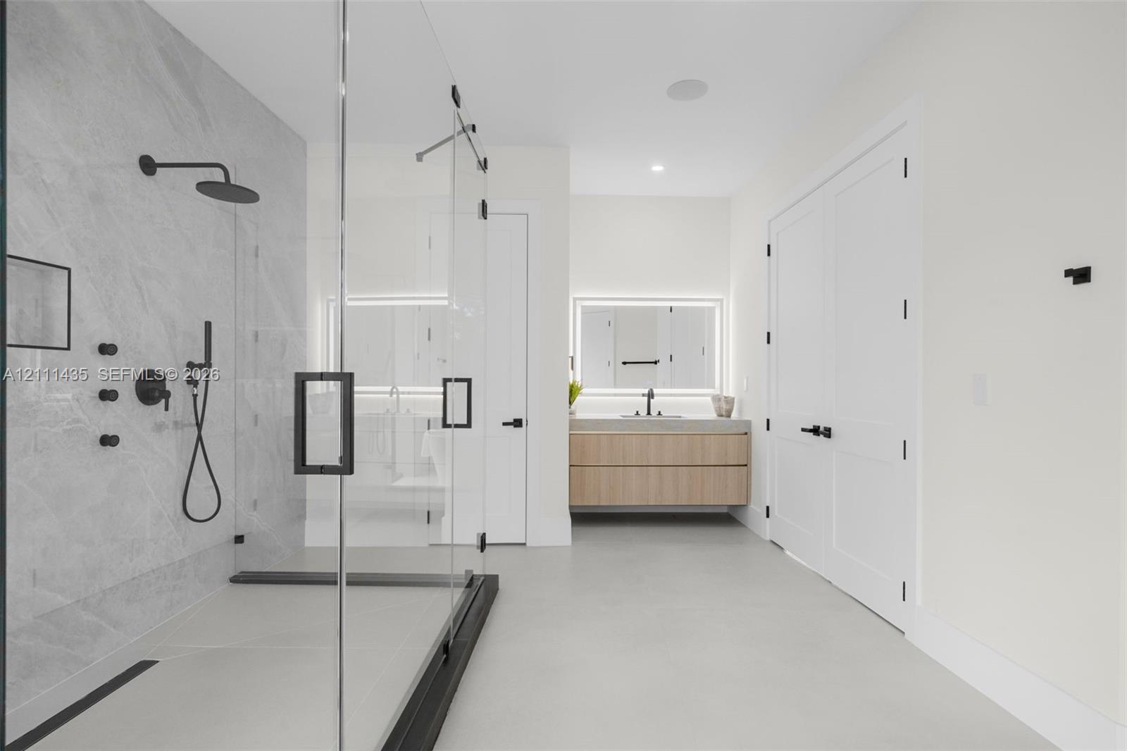 Walk-in shower with frameless glass enclosure, rainfall shower head, and stone-tile surround, paired with a floating wood-finish vanity featuring an integrated LED-backlit mirror