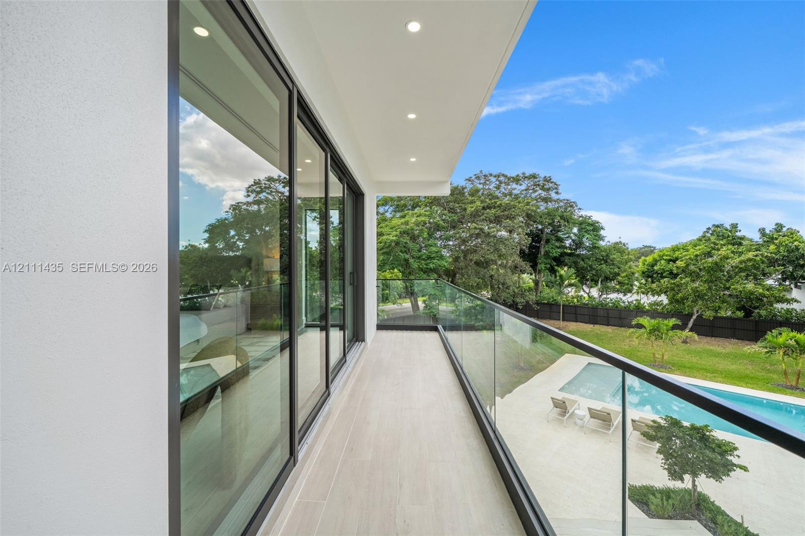 Covered balcony featuring expansive sliding glass doors, frameless glass railings, recessed lighting, and tile flooring